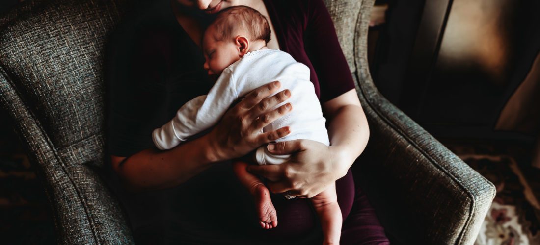 Mom sitting in a chair holding new newborn baby during a San Diego in-home lifestyle newborn photo session by Love Michelle Photography