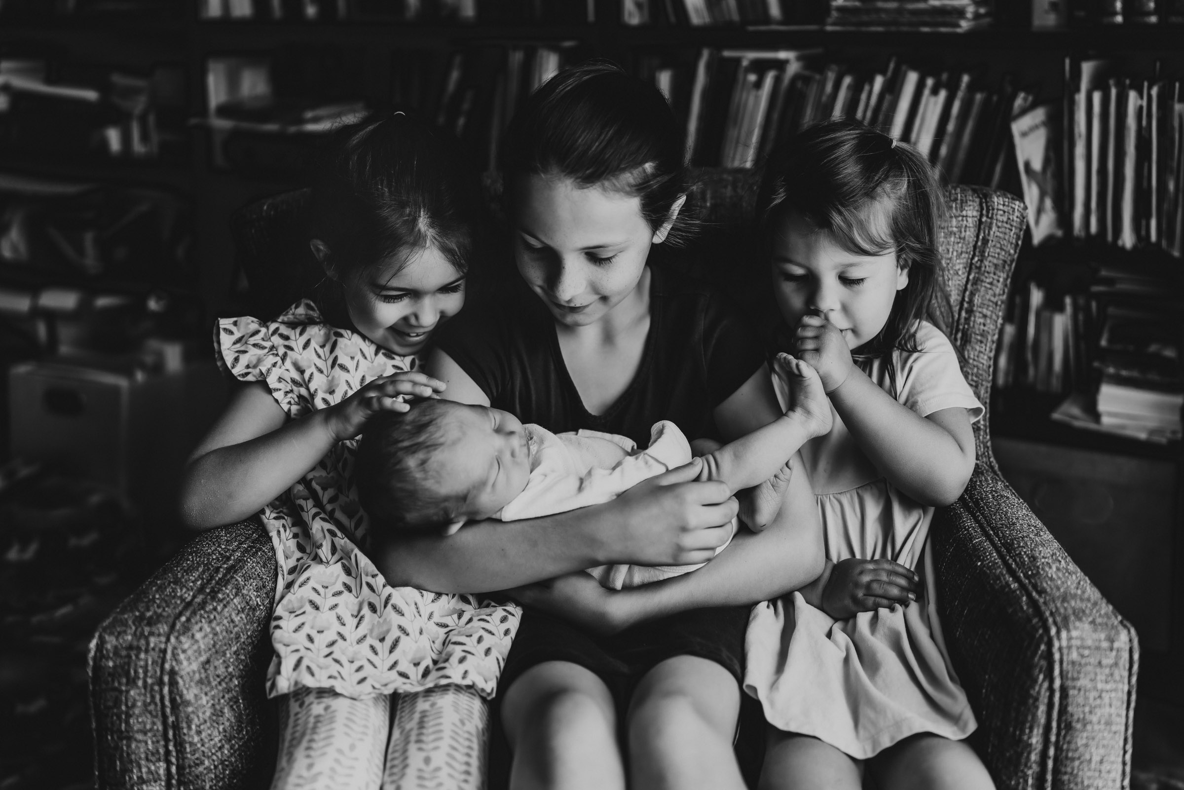 3 little girls holding their new baby sister during a San Diego in-home lifestyle newborn session by Love Michelle Photography
