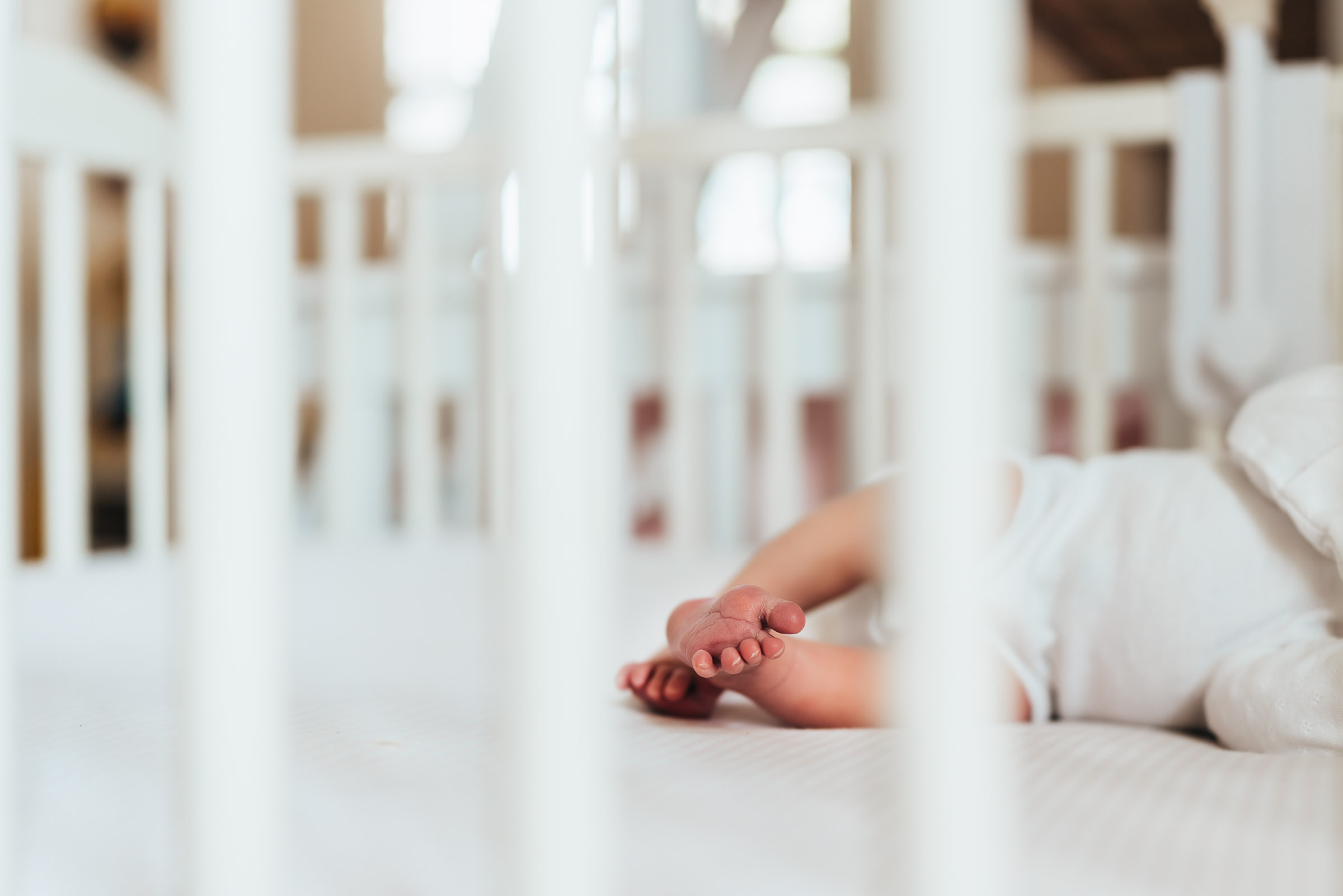 Little newborn baby feet through the crib slats, photographer during a San Diego in-home lifestyle newborn session by Love Michelle Photography