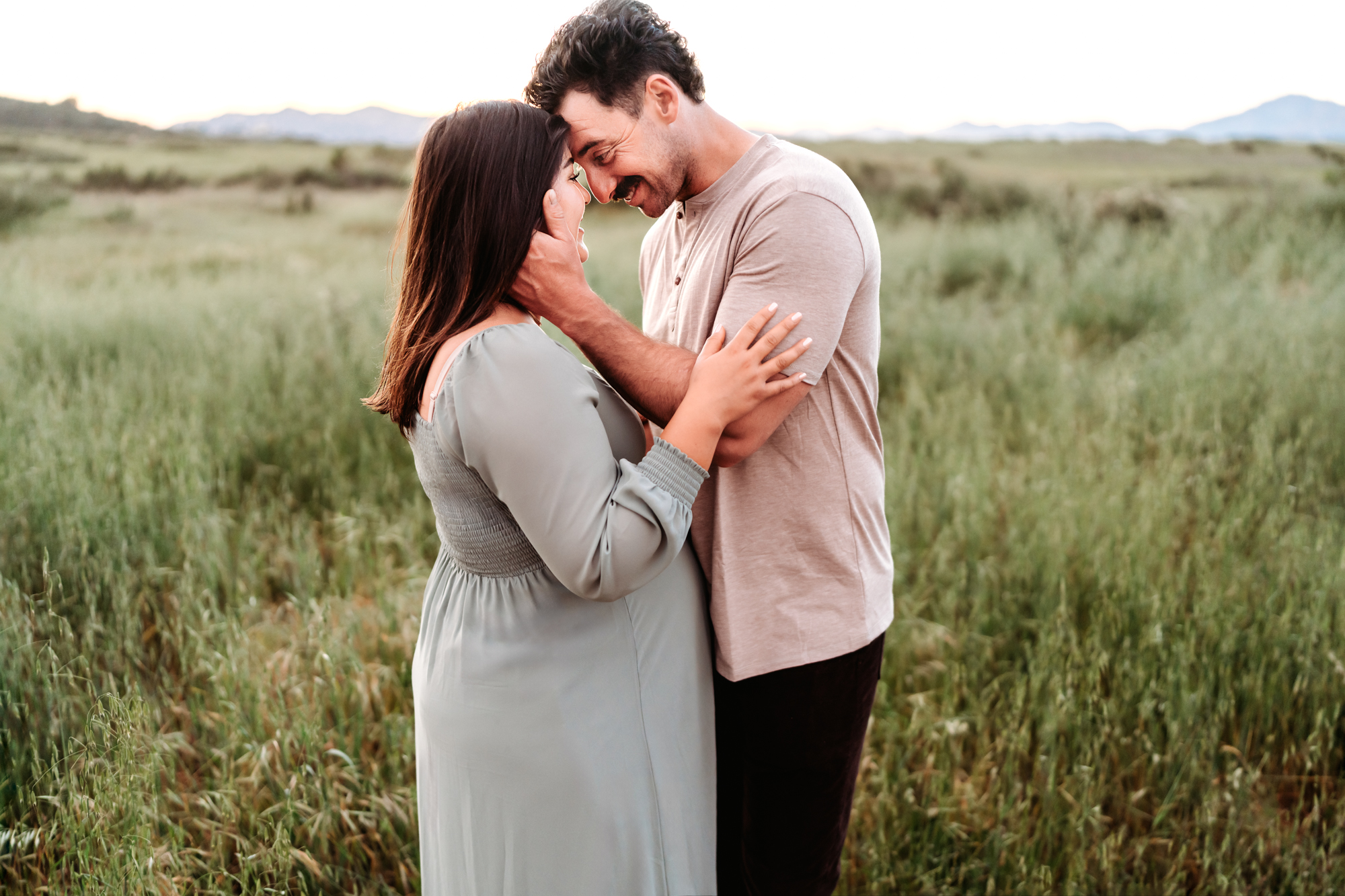A man embraces his pregnant wife during their San Diego maternity photoshoot with Love Michelle Photography.