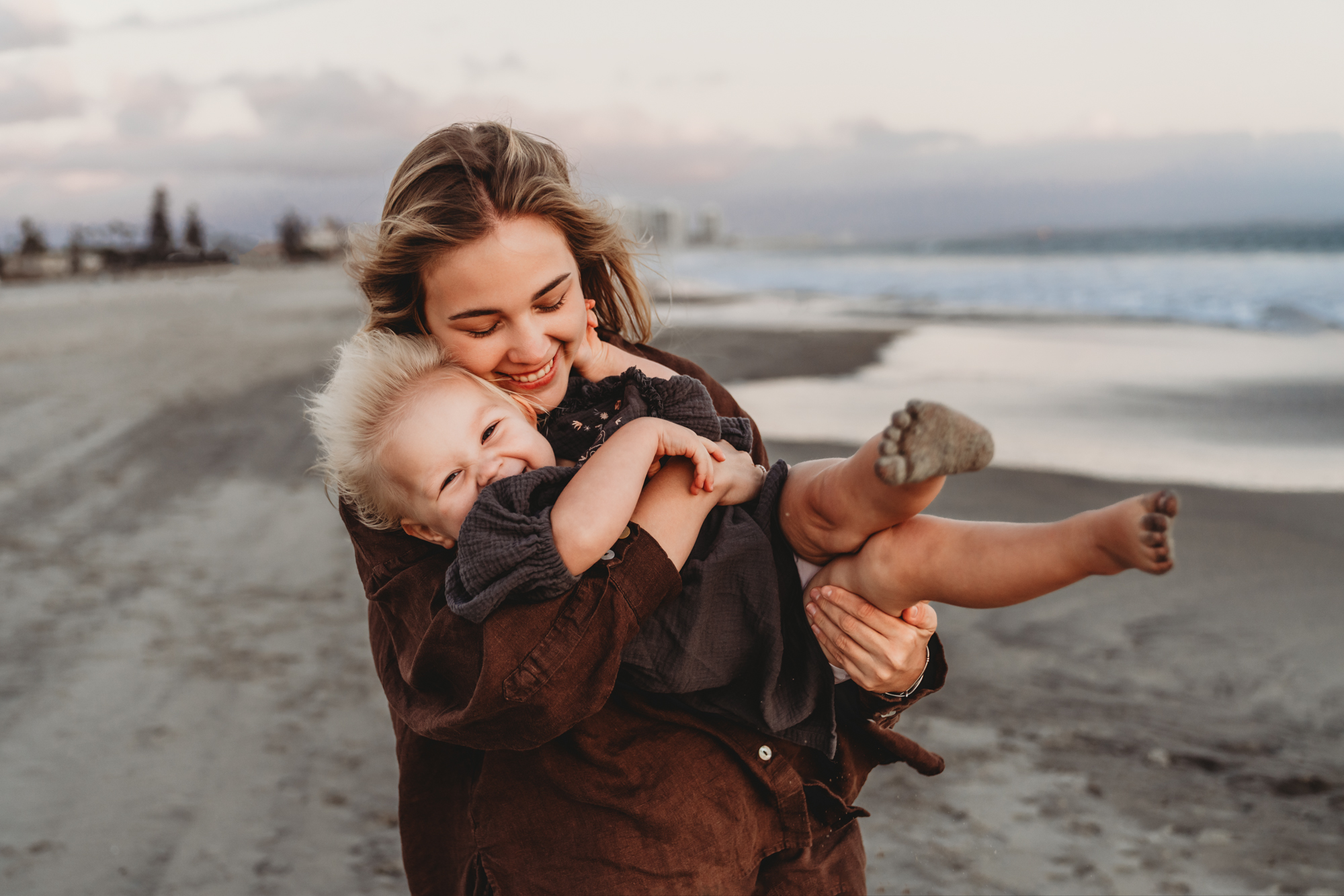 During a Coronado beach family photoshoot, a mom hold her toddler daughter while they both laugh.
