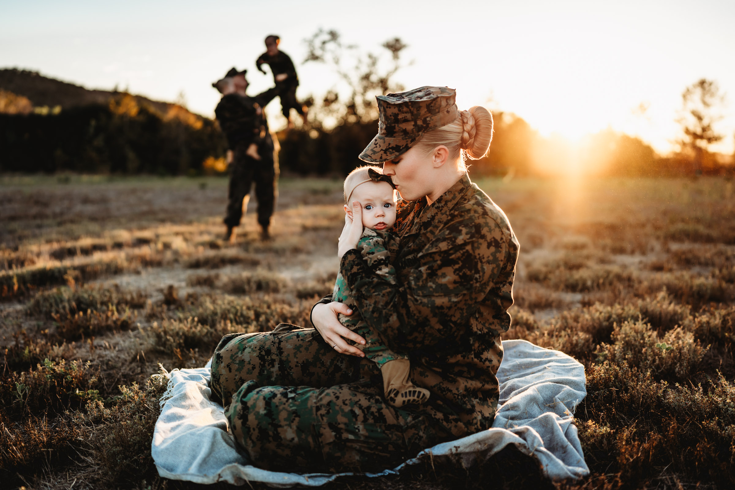 Marine Corp mom sitting in San Diego field kissing baby during family photo session