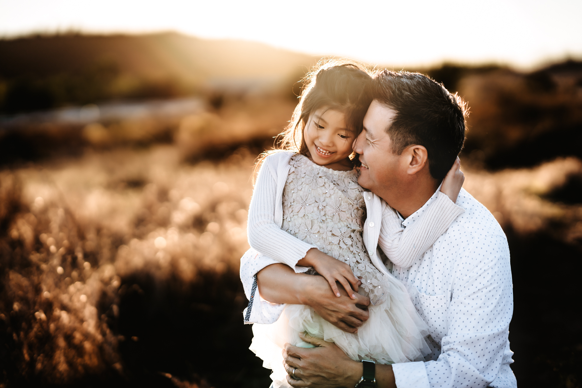 A father hugs his young daughter in a golden San Diego field during a fall family photo session by Love Michelle Photography. 