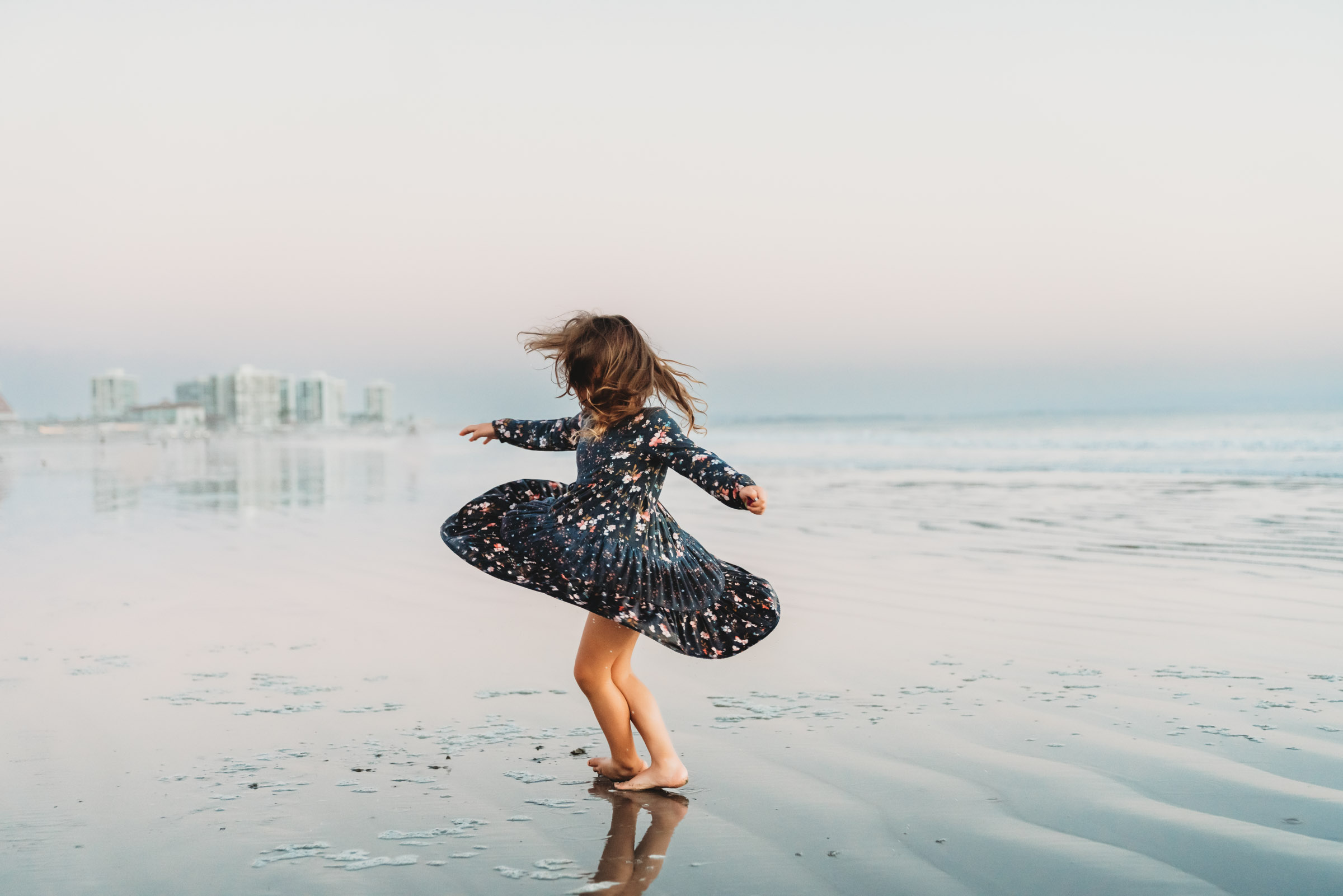 Little girl twirling in a blue dress on Coronado Beach during a lifestyle family photography session on Coronado Beach.