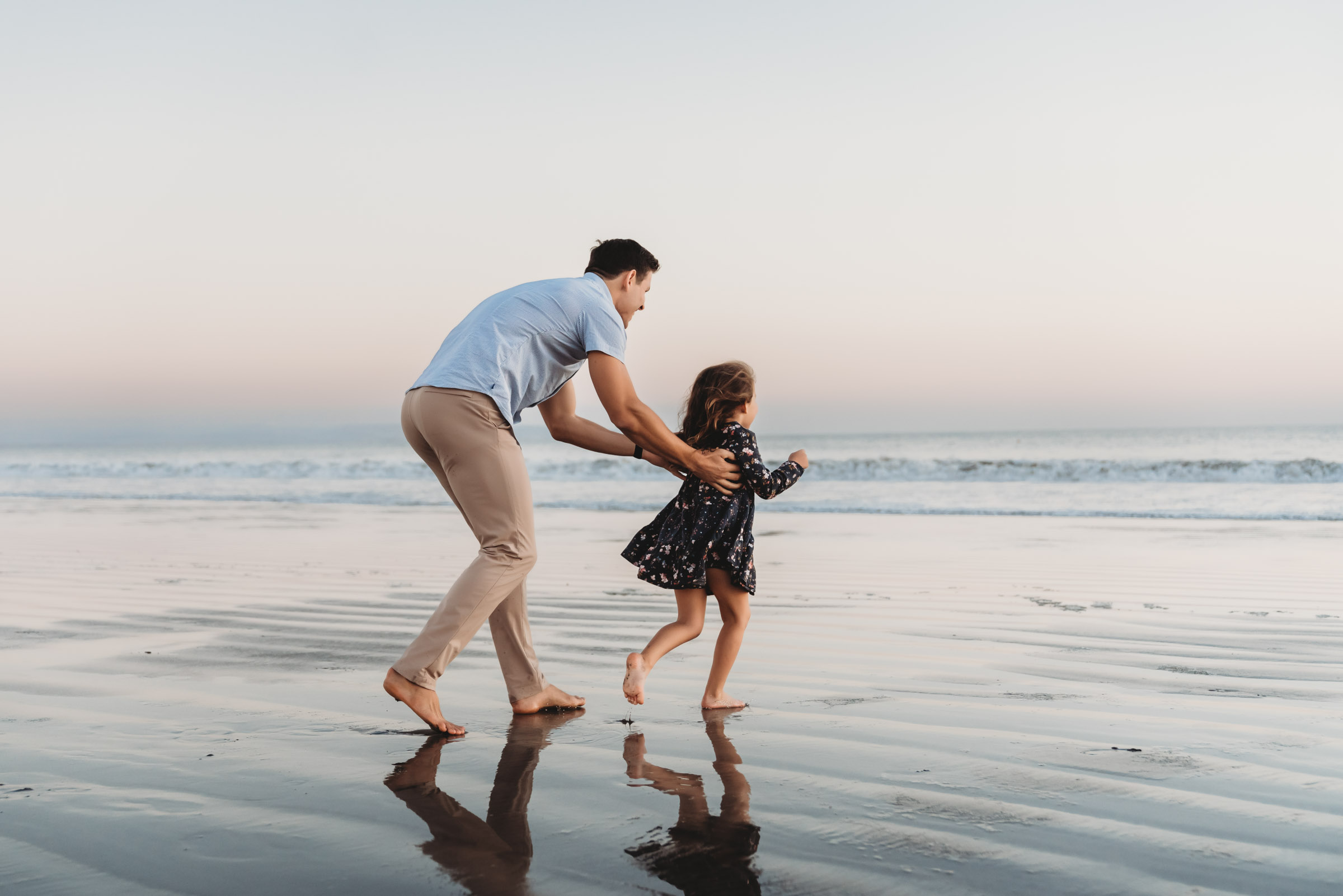 Daughter running on sand away from her father during a lifestyle family photography session on Coronado Beach.