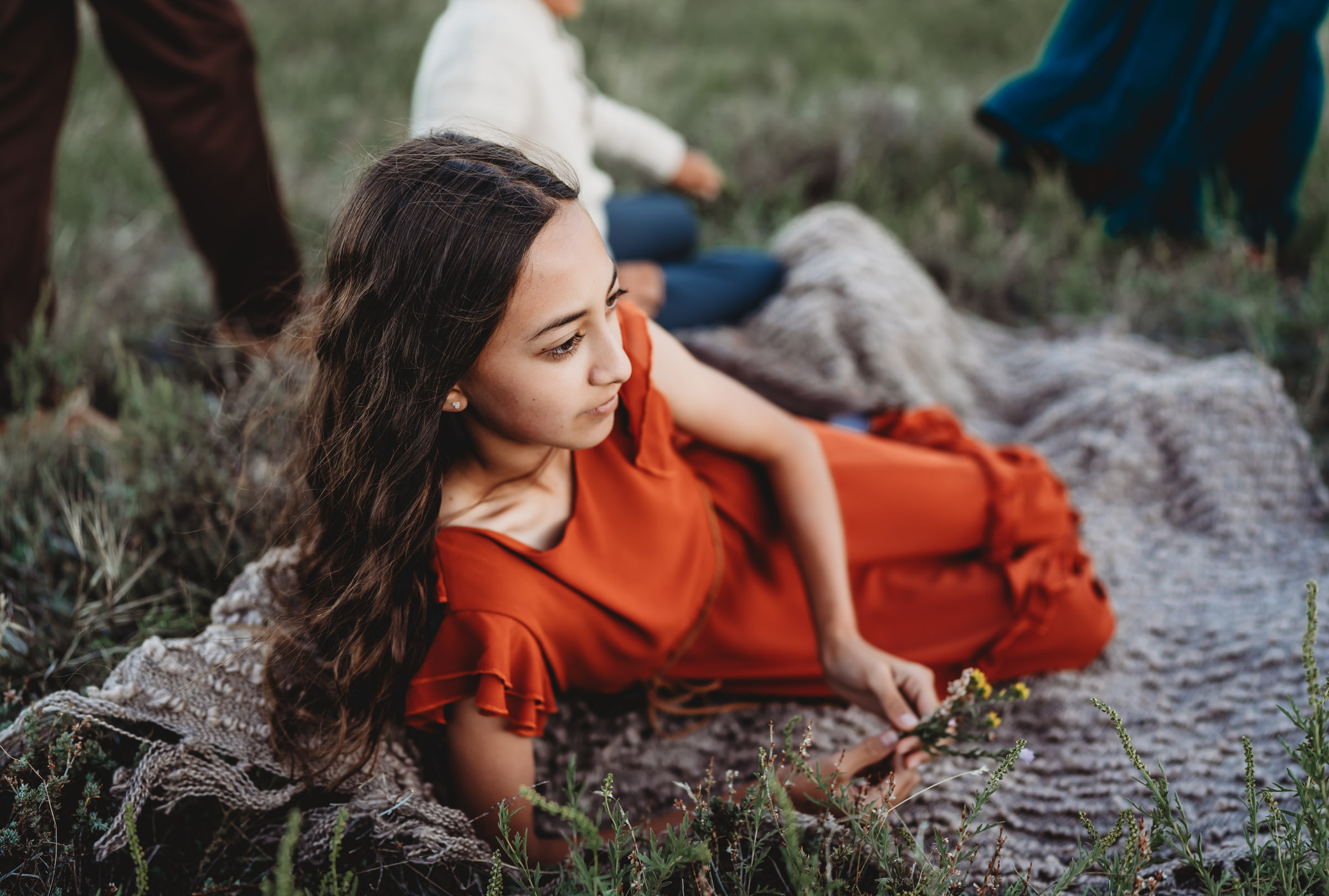 Long haired girl in an orange dress reclining in a Mt. Laguna meadow during a family photography session.