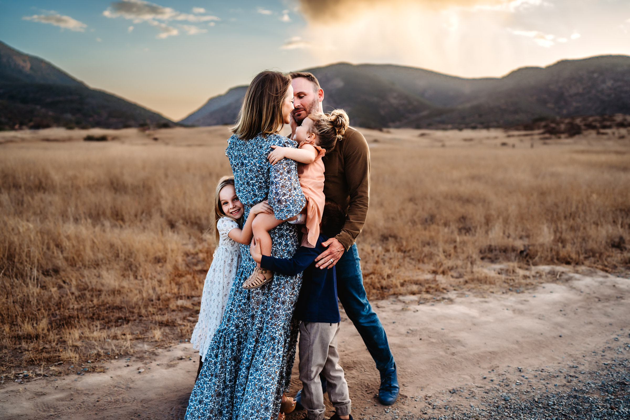 Couple embracing while holding their children in a field during a lifestyle photography session in Mission Trails Regional Park 