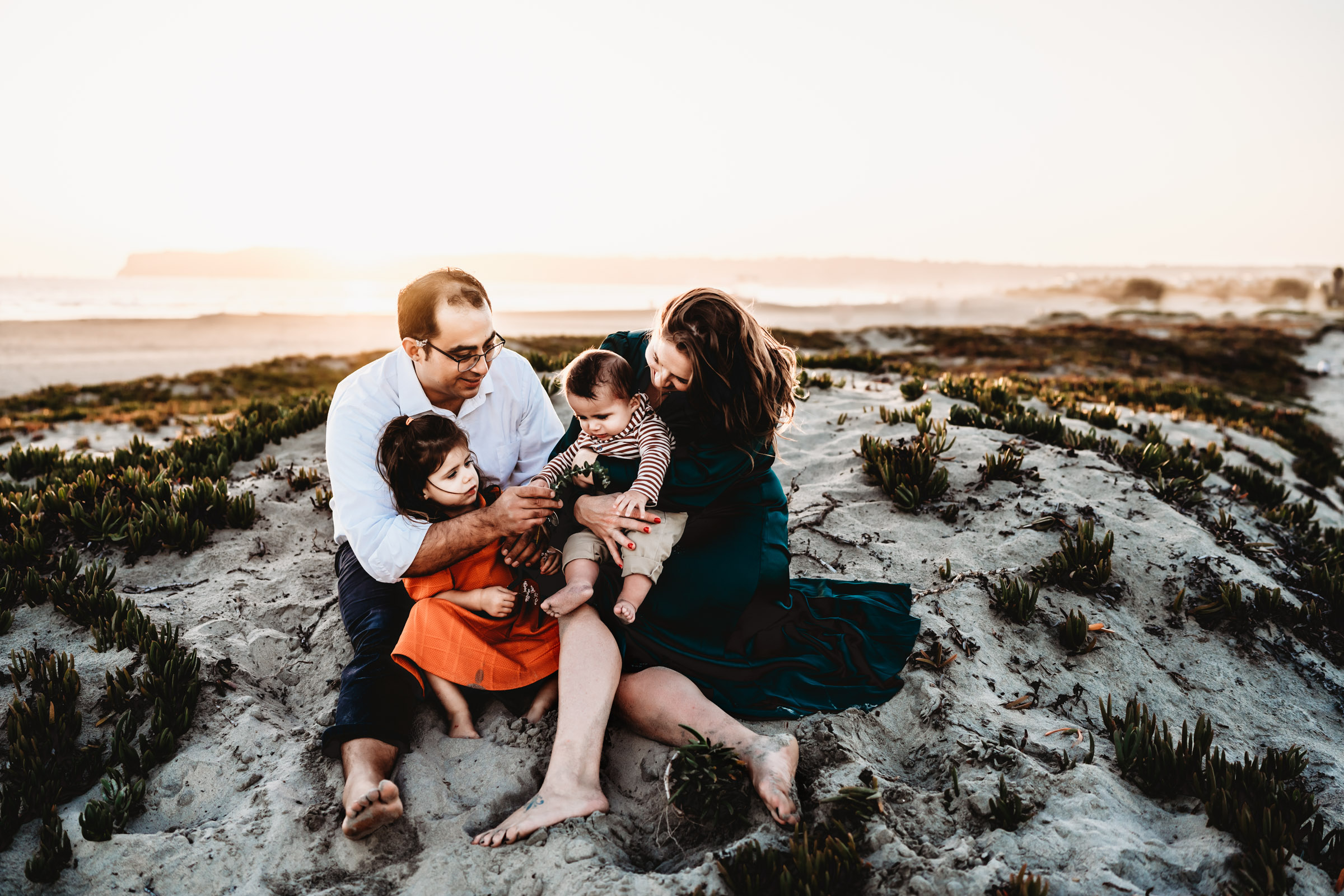 A family sitting on a sand dune during a lifestyle family photography session on Coronado Beach. 