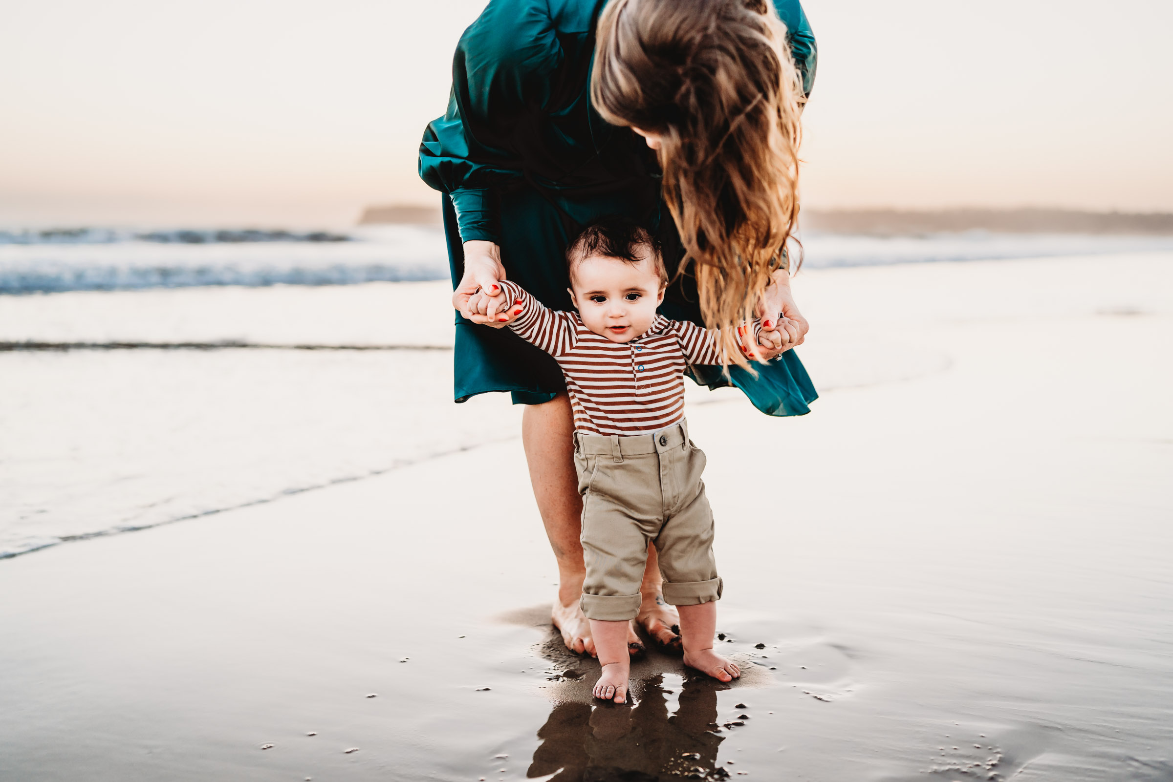 Mom holding baby boy's hands on Coronado Beach during a lifestyle family photography session. 