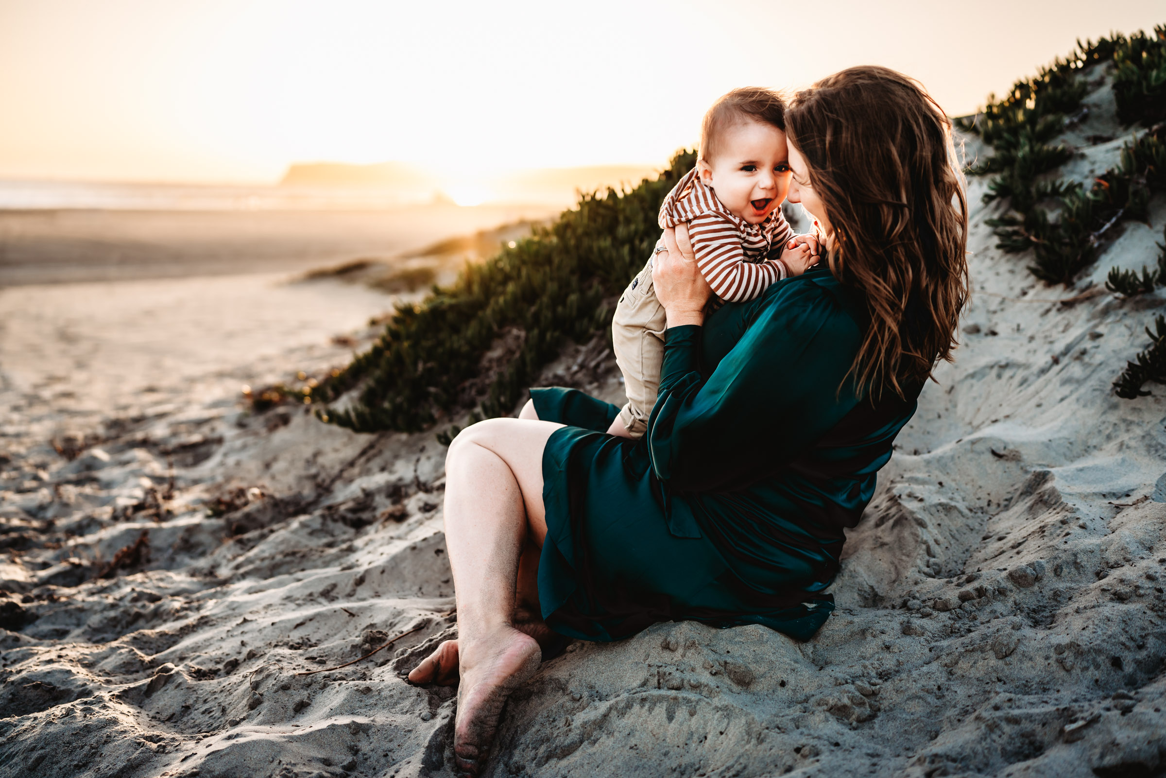Mom sitting in the sand holding her baby boy during a lifestyle family photography session on Coronado Beach. 