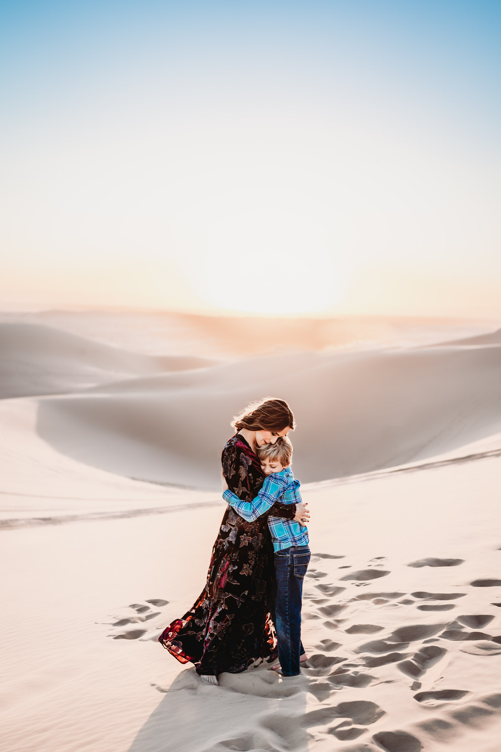 A mom hugging her son on a sand dune during a lifestyle family photography session at the Imperial Sand Dunes in Glamis, California. 