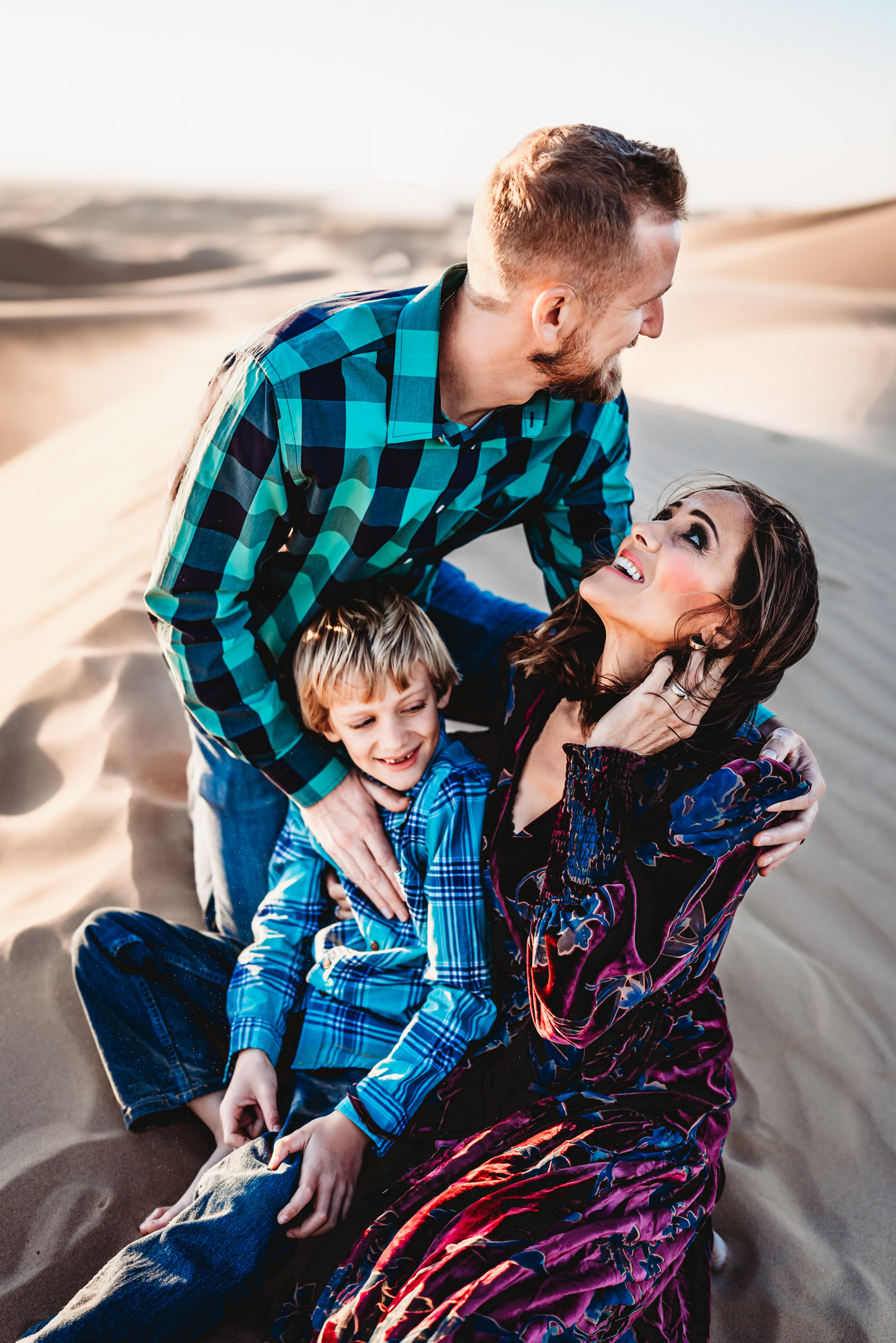 A family of 3 sitting on a sand dunes during a lifestyle family photography session at the Imperial Sand Dunes in Glamis, California. 