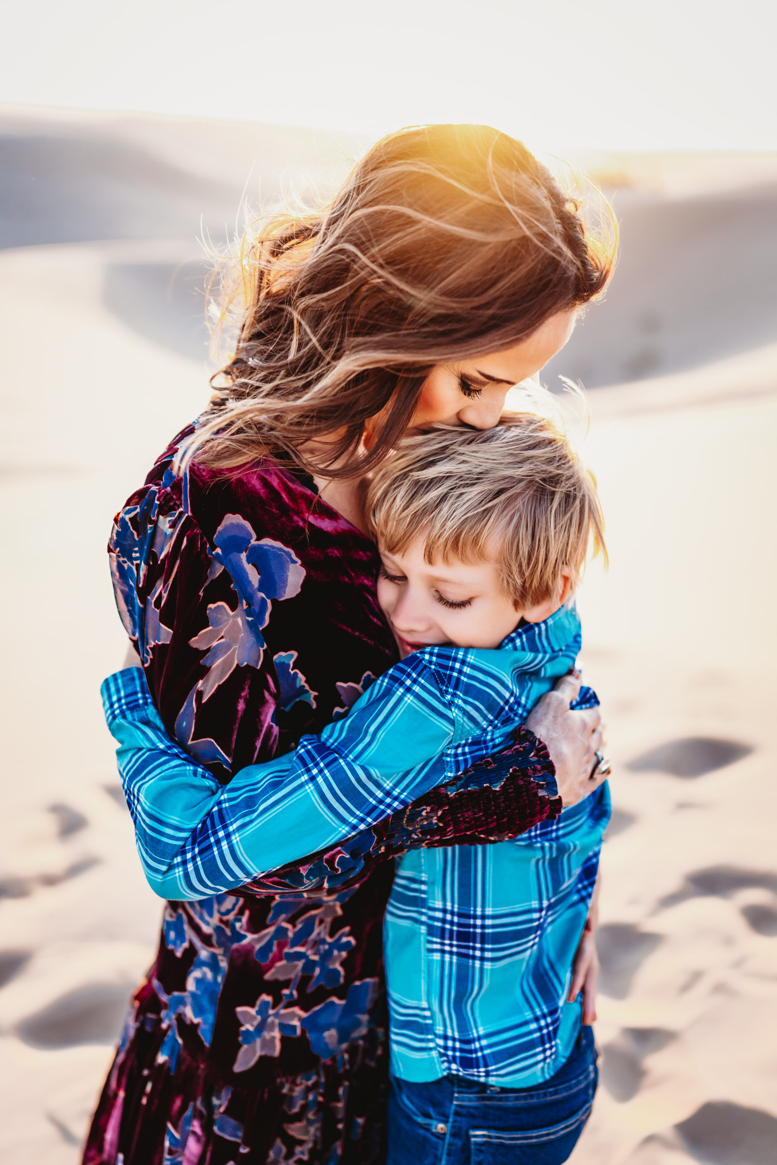 A woman hugging and kissing her son on a sand dune during a lifestyle family photography session at the Imperial Sand Dunes in Glamis, California. 