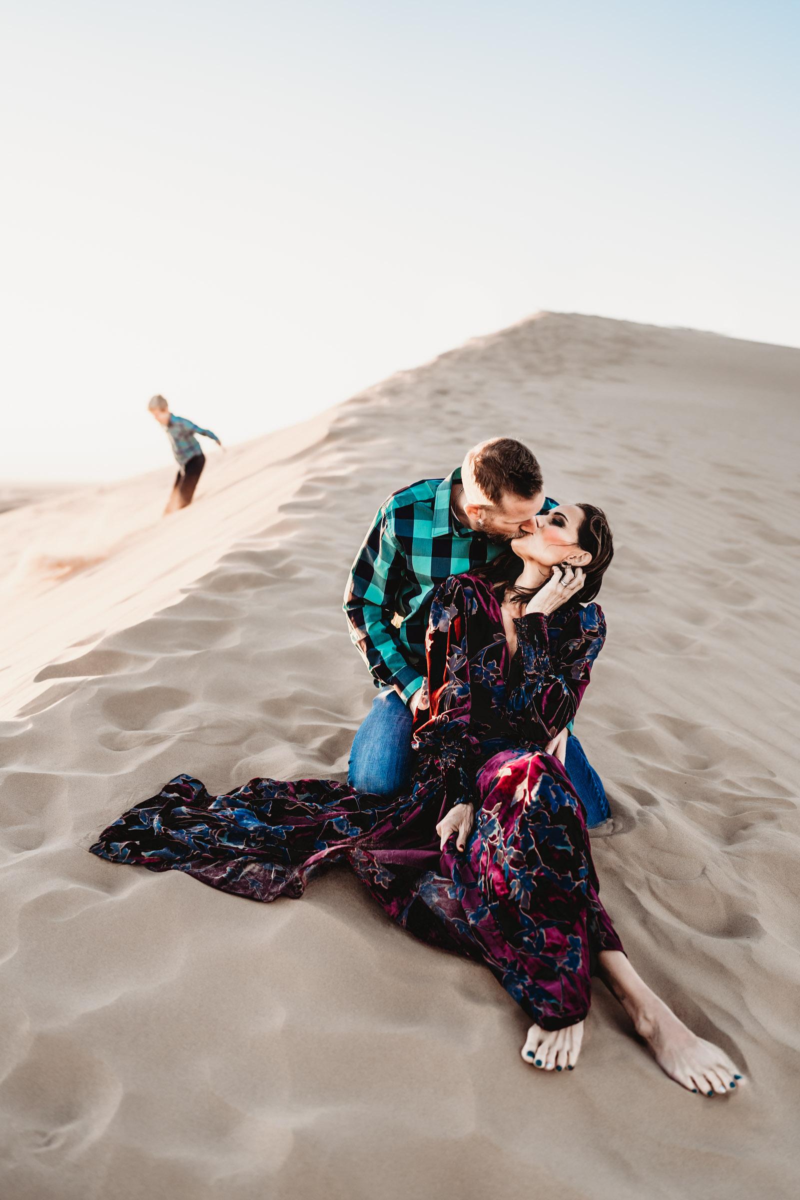 Man and woman sitting and kissing on the Imperial Sand Dunes during a San Diego lifestyle family photography session. 