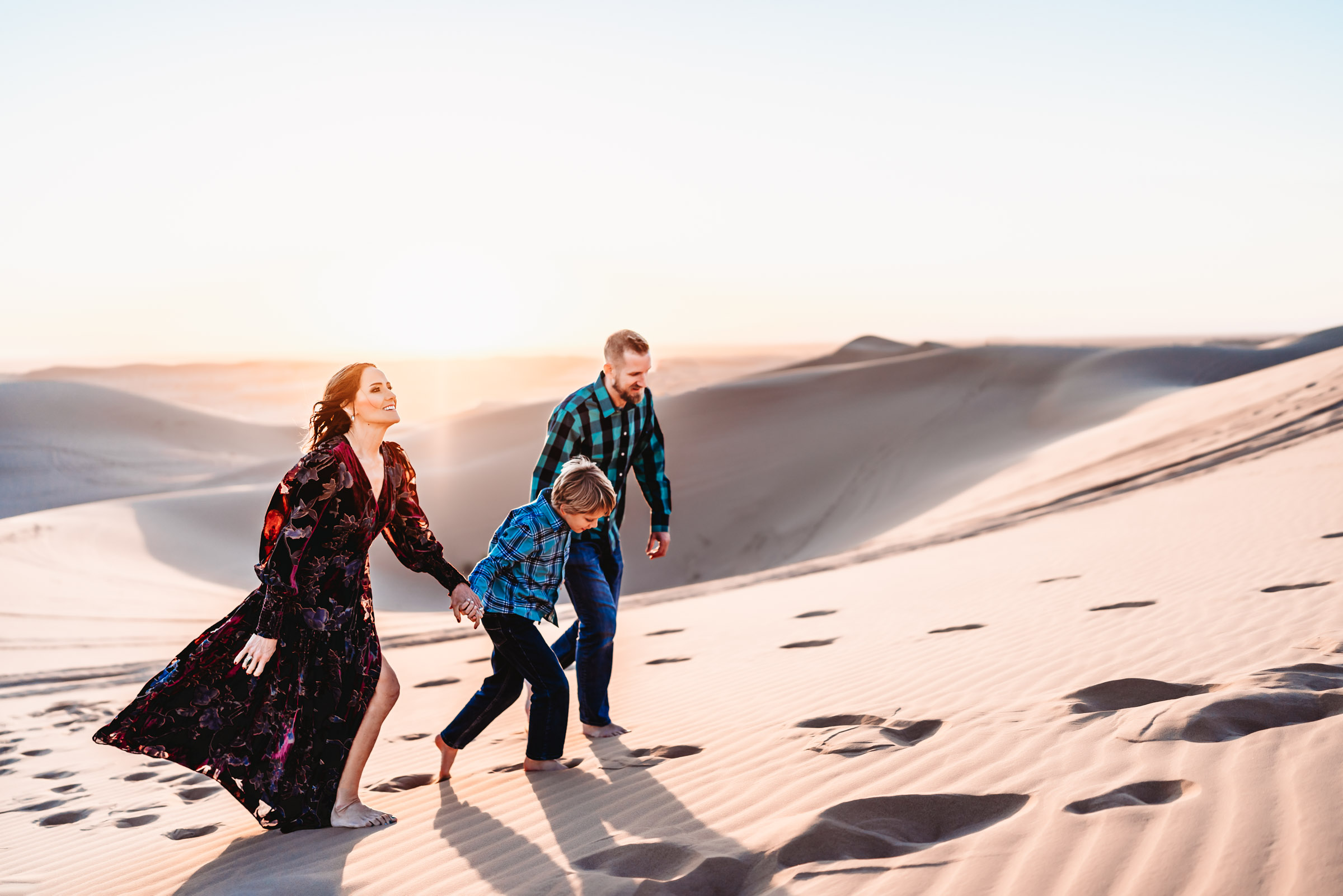 Family holding hands and walking up a sand dune on the Imperial Sand Dunes during a San Diego lifestyle family photography session. 