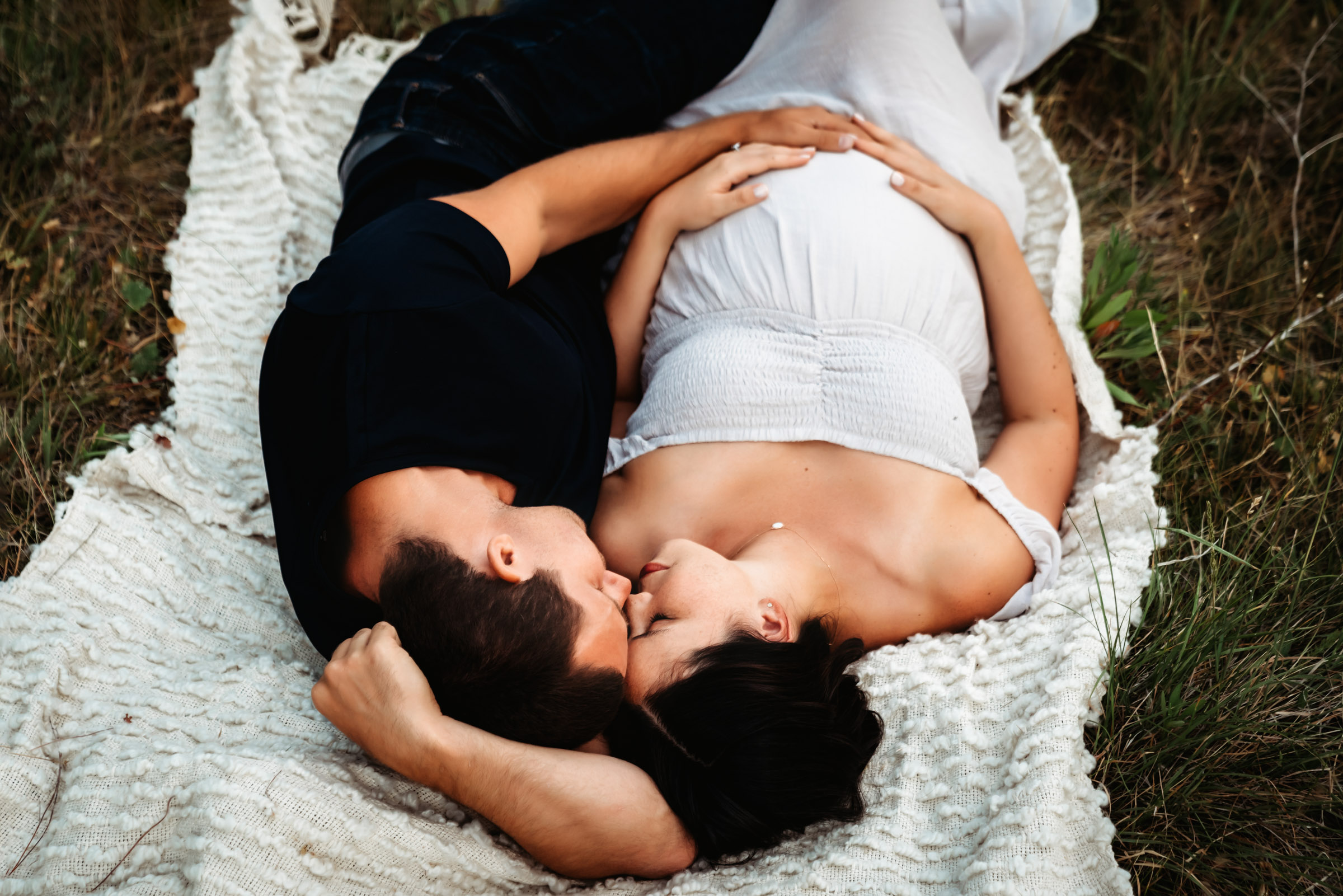 A pregnant woman and her husband snuggling on a blanket during a San Diego lifestyle maternity photo session.