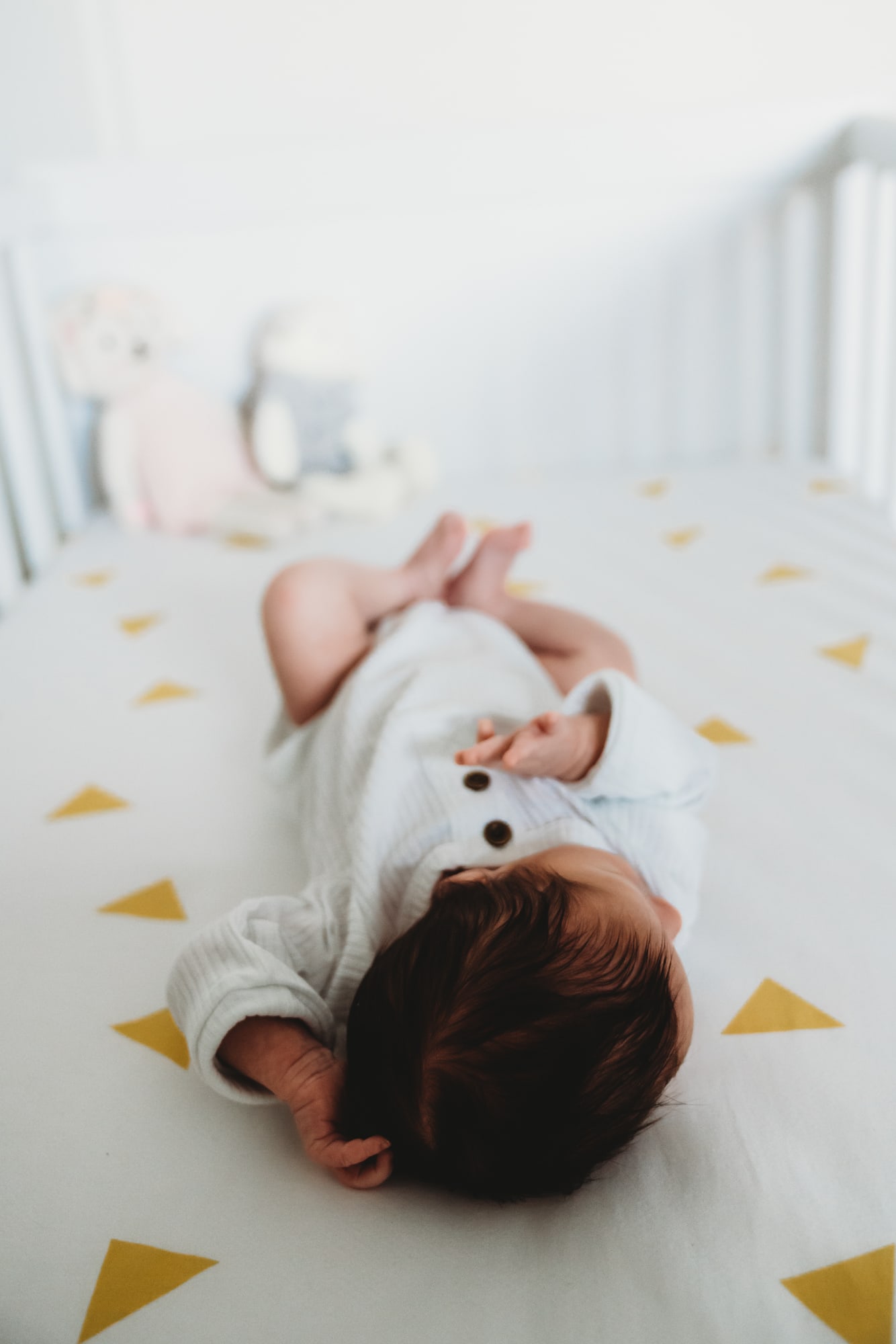 A newborn laying in her crib wearing a white onesie during a San Diego newborn photo session