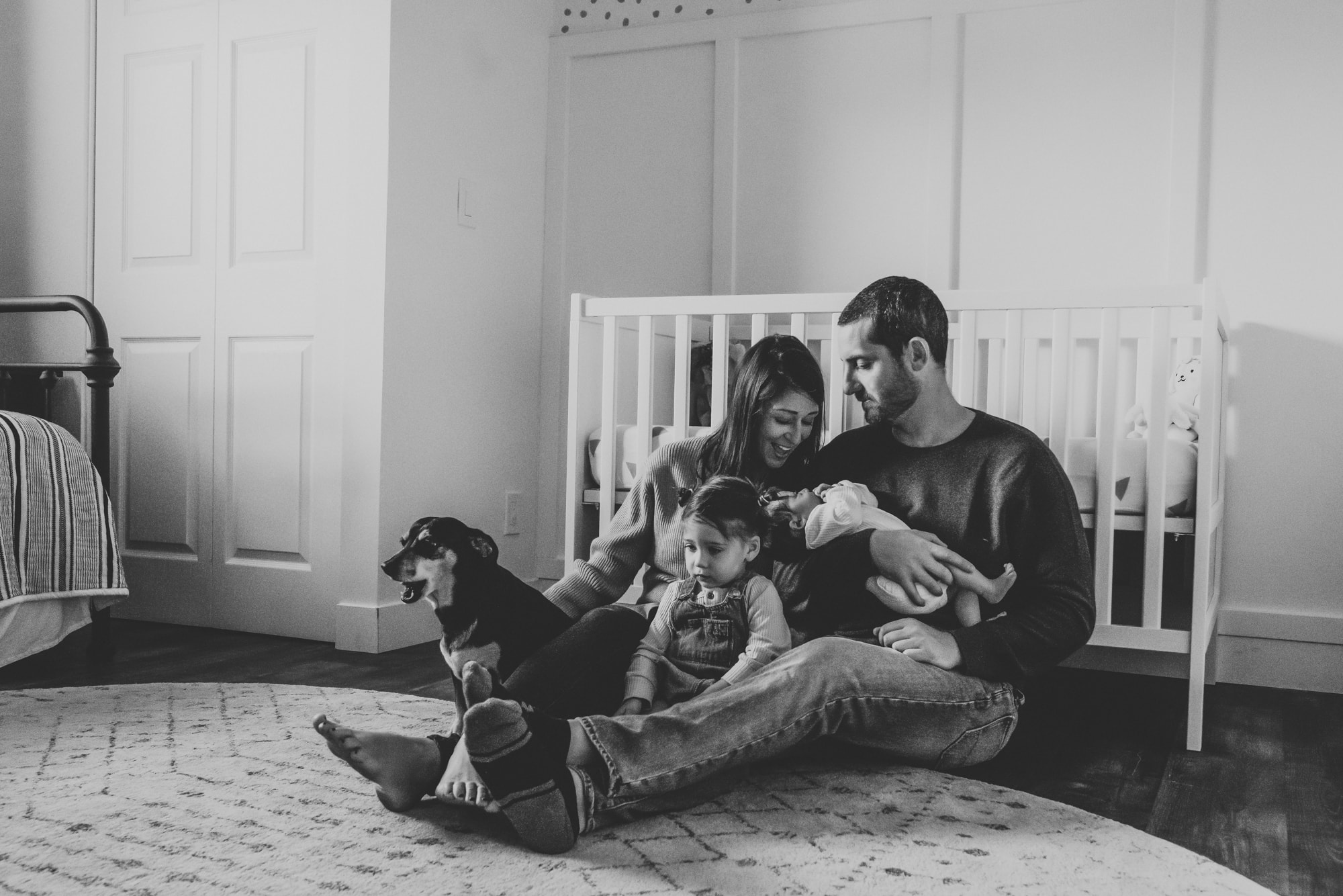 A family sitting on the floor with their dog and newborn baby during a San Diego in-home photo session by Love Michelle Photography