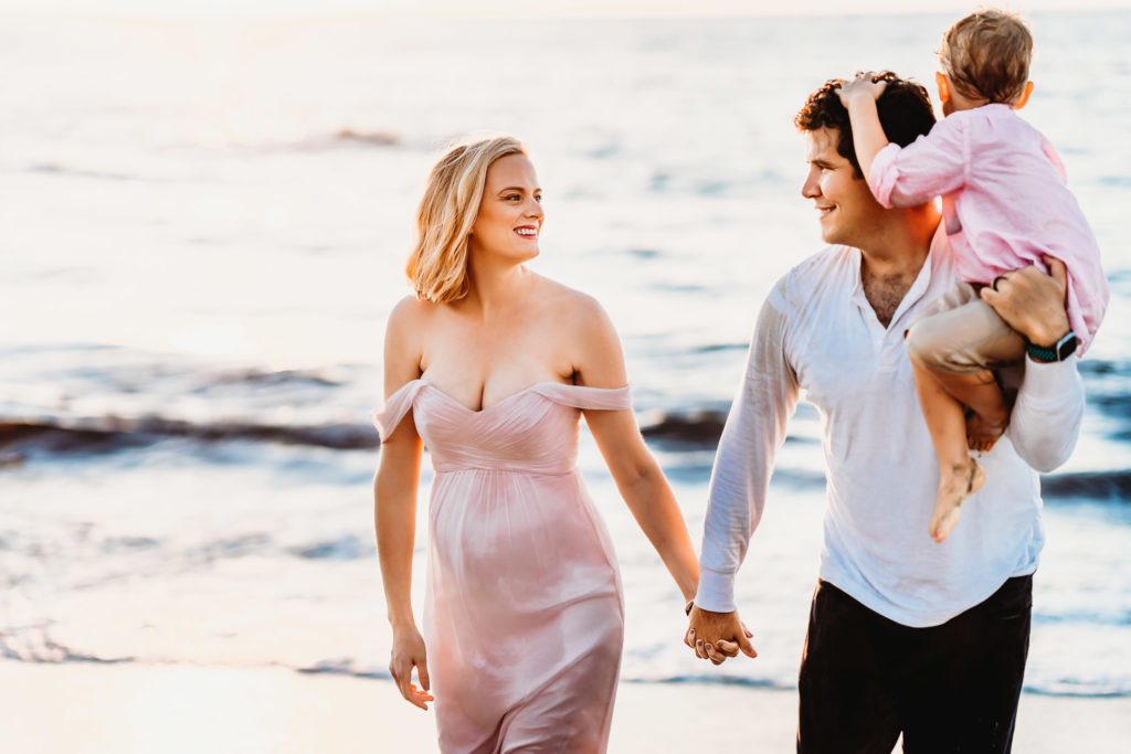 Pregnant woman and husband holding hands and walking on a La Jolla Beach during a San Diego lifestyle maternity photo session  by Love Michelle Photography. 