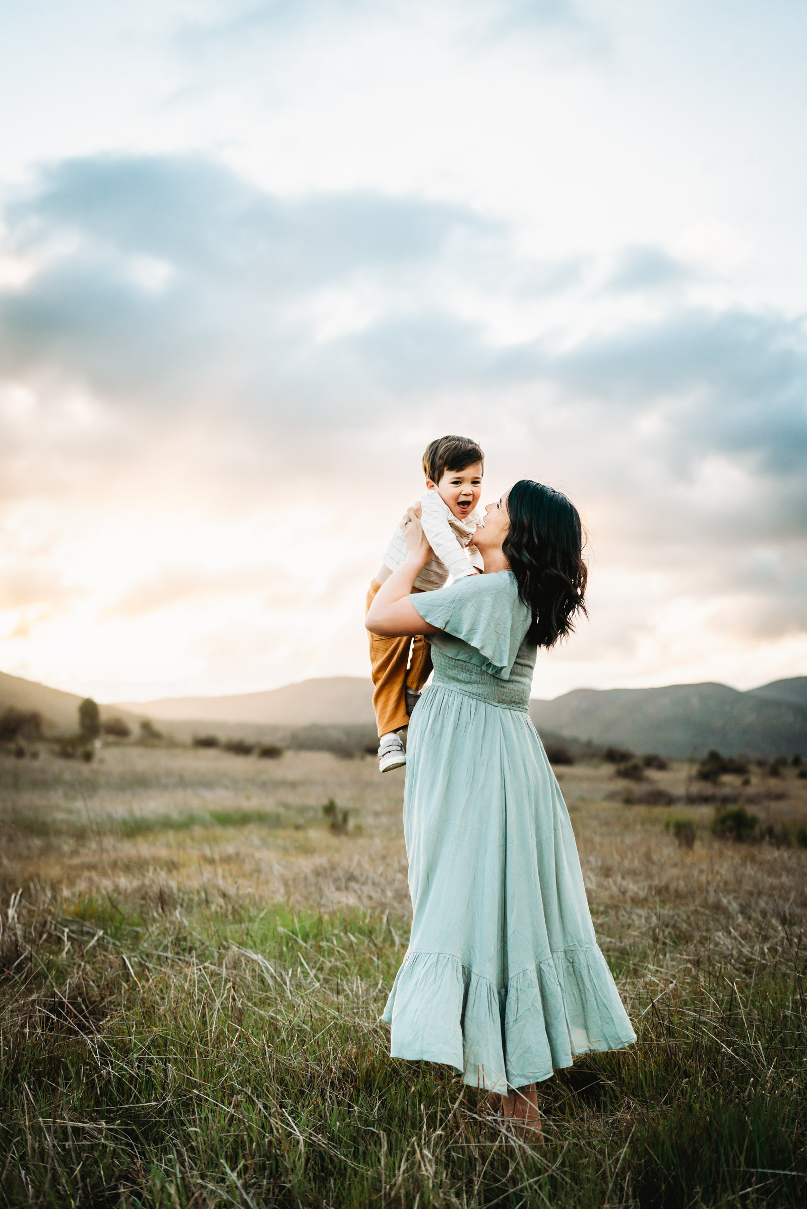 Pregnant woman holding her little boy on a field in Mission Trails Regional Park during a San Diego lifestyle maternity photo session.