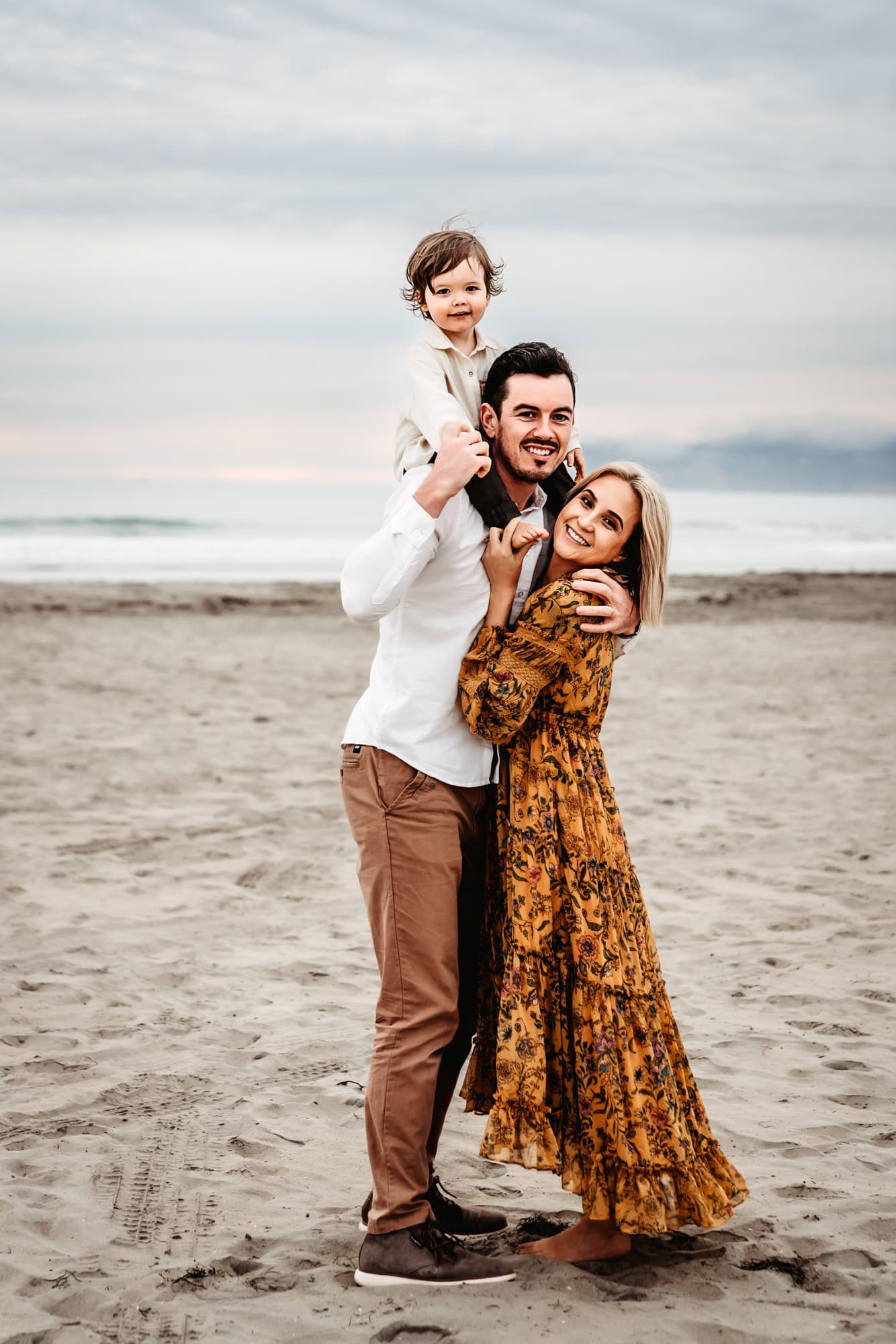 Family of three on Coronado Beach smiling at the camera during a family photo session in San Diego.