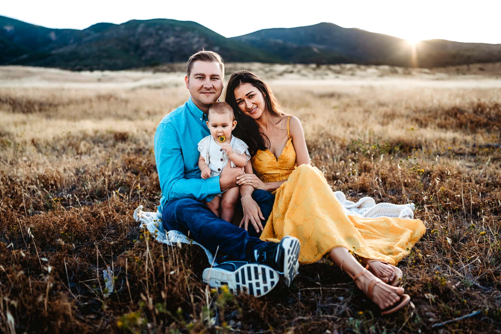 Family of three sitting in a field during a family photo session in San Diego.