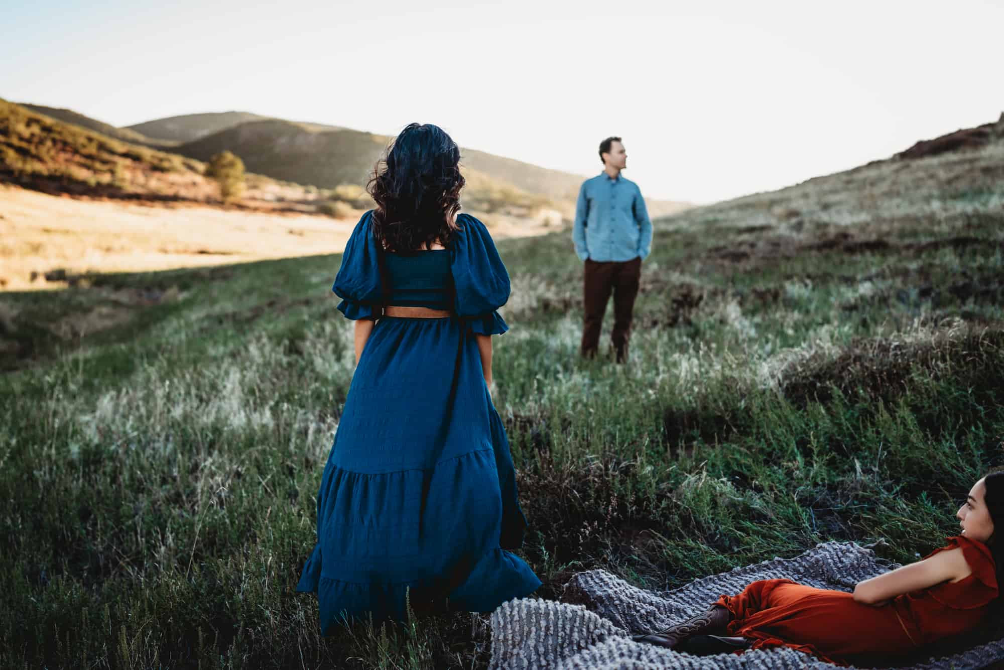 A woman wearing a long blue dress standing in a Mt. Laguna field looking at her husband during a San Diego lifestyle family photography session by Love Michelle Photography