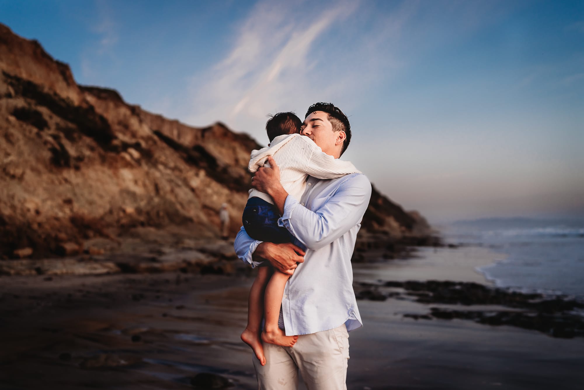 A father embracing his 3 year old son on a beach in Del Mar, California. 