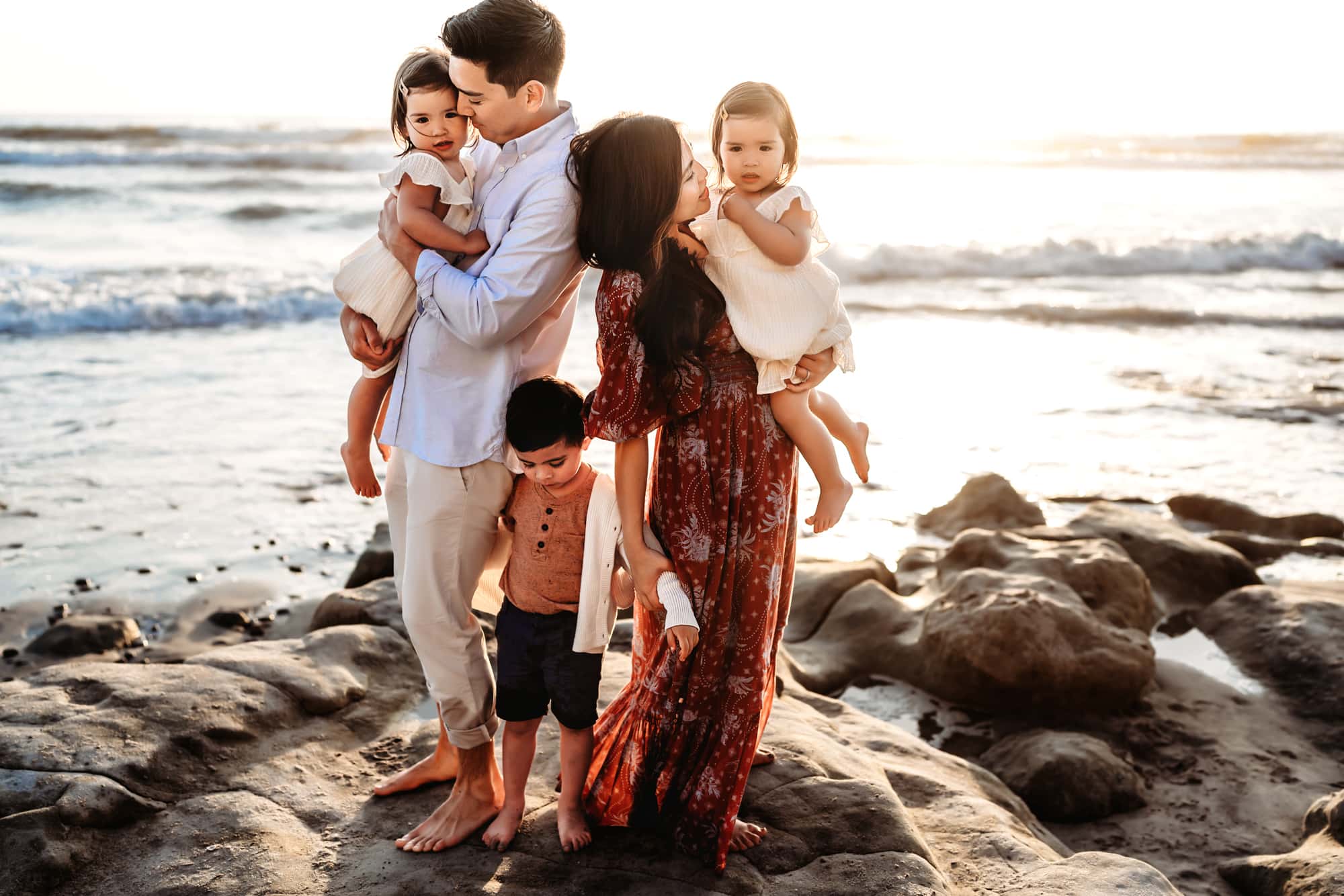 A family of five standing on a large rock together on a Del Mar beach during a lifestyle family photography session.