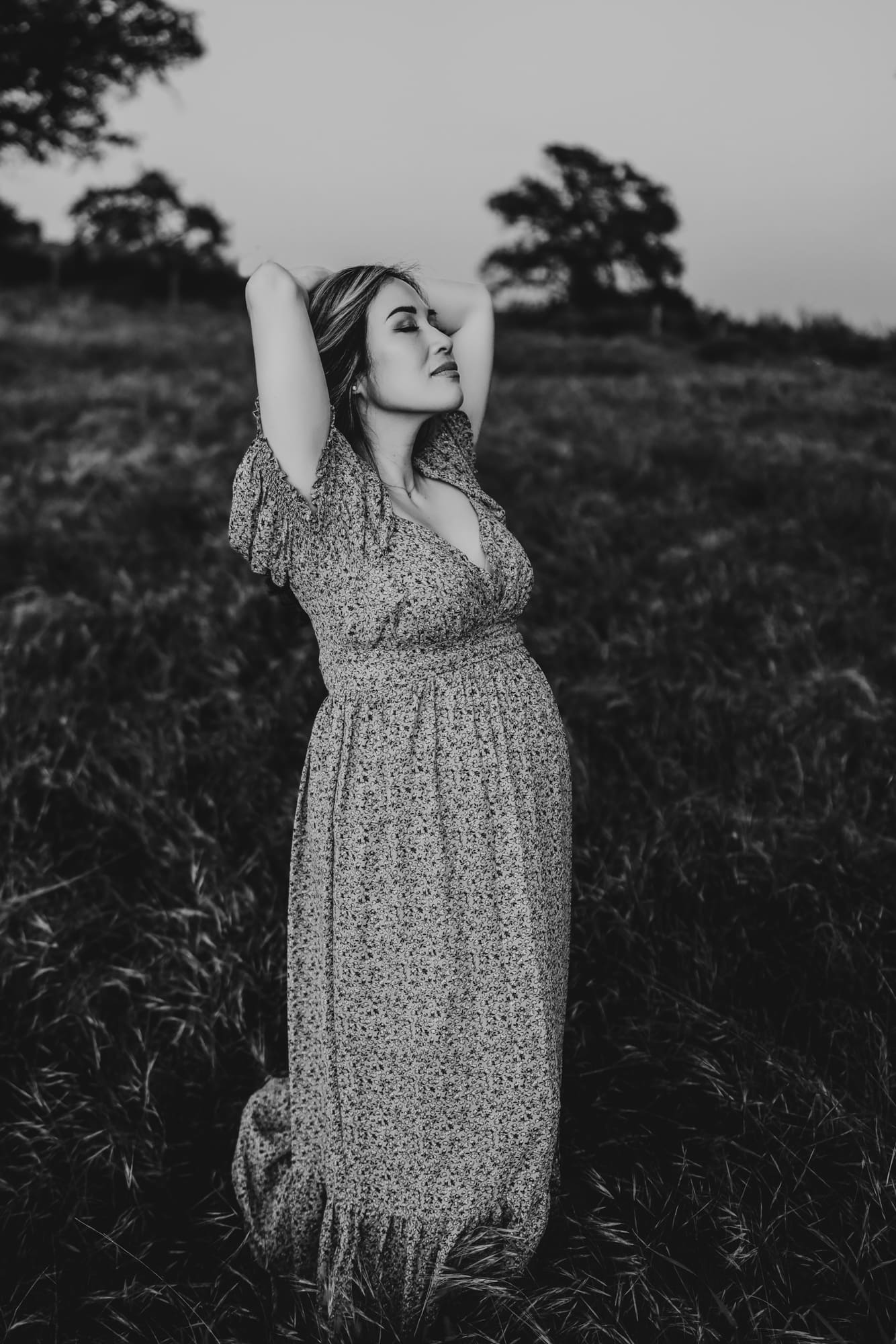 A black and white image of a pregnant woman closing her eyes with her head lifted to the sky in a field of grass, during a lifestyle maternity session by Love Michelle Photography. 