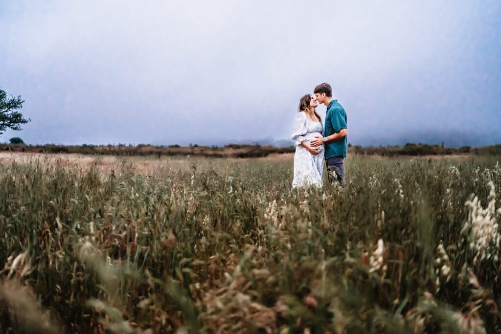 A pregnant woman kisses her husband in a field during a maternity photography session in Southern California.