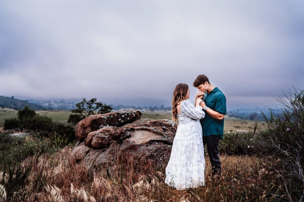 A man kisses his pregnant wife's hands during their maternity photography session in San Diego.