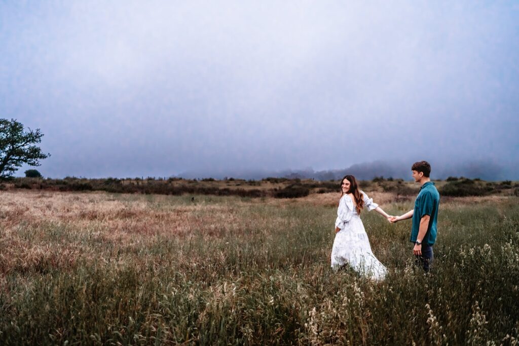 A pregnant woman leads her husband into a field during a maturity photo session in San Diego