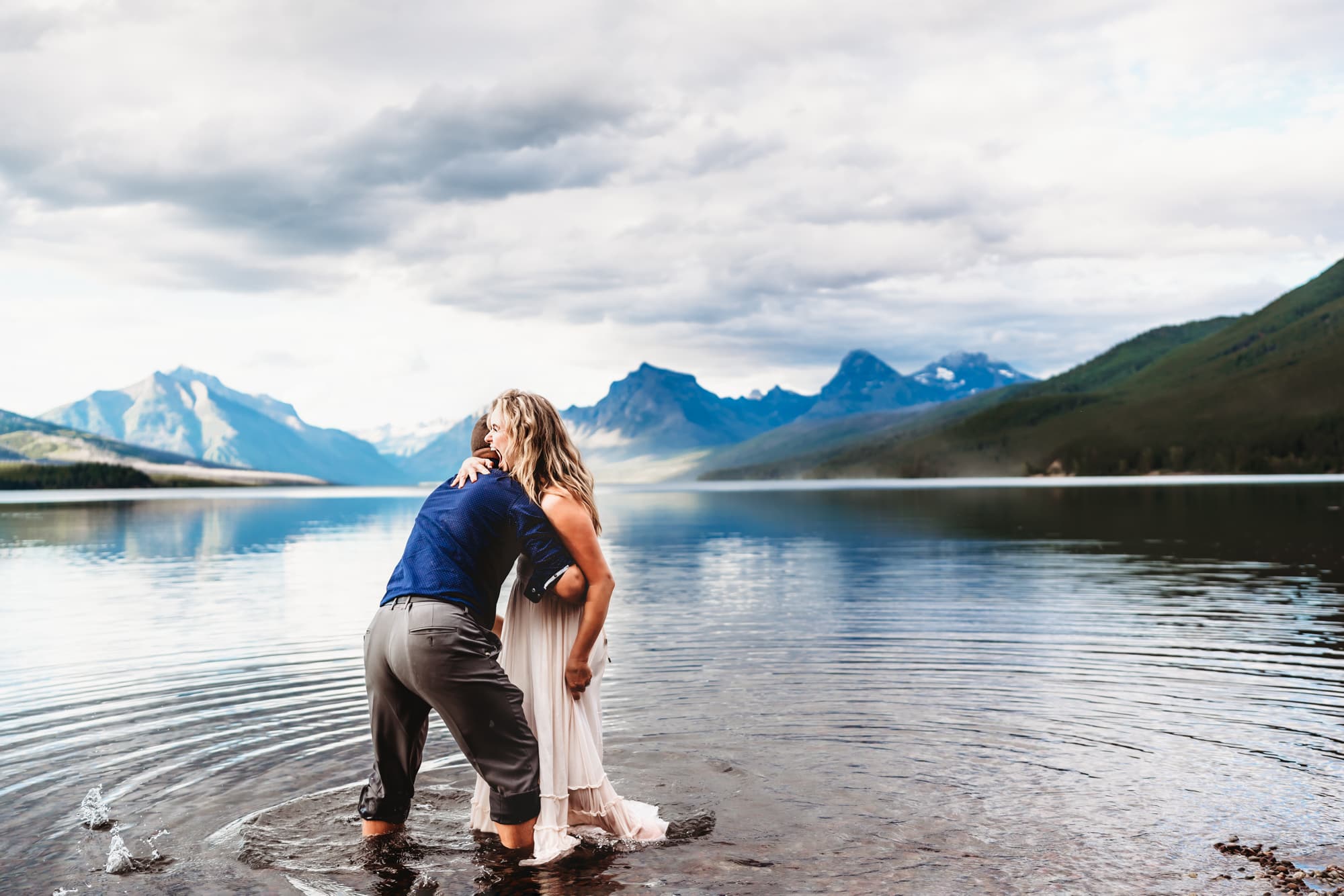 A couple plays together on the shores of Montana's Lake McDonald during a travel family photography session by vacation photographer Love Michelle Photography. 