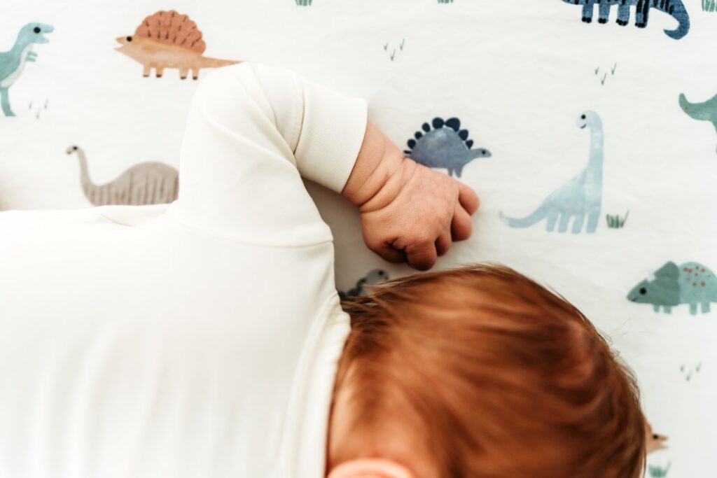 A newborn baby with red hair laying on a sheet covered in dinosaurs.