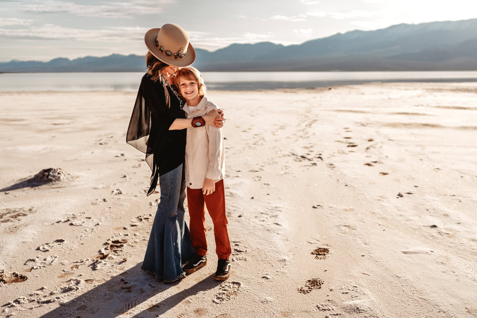 A woman stand in Death Valley's Badwater Basin, holding on to her 10 year old son and smiling as he looks at the camera and smiles.