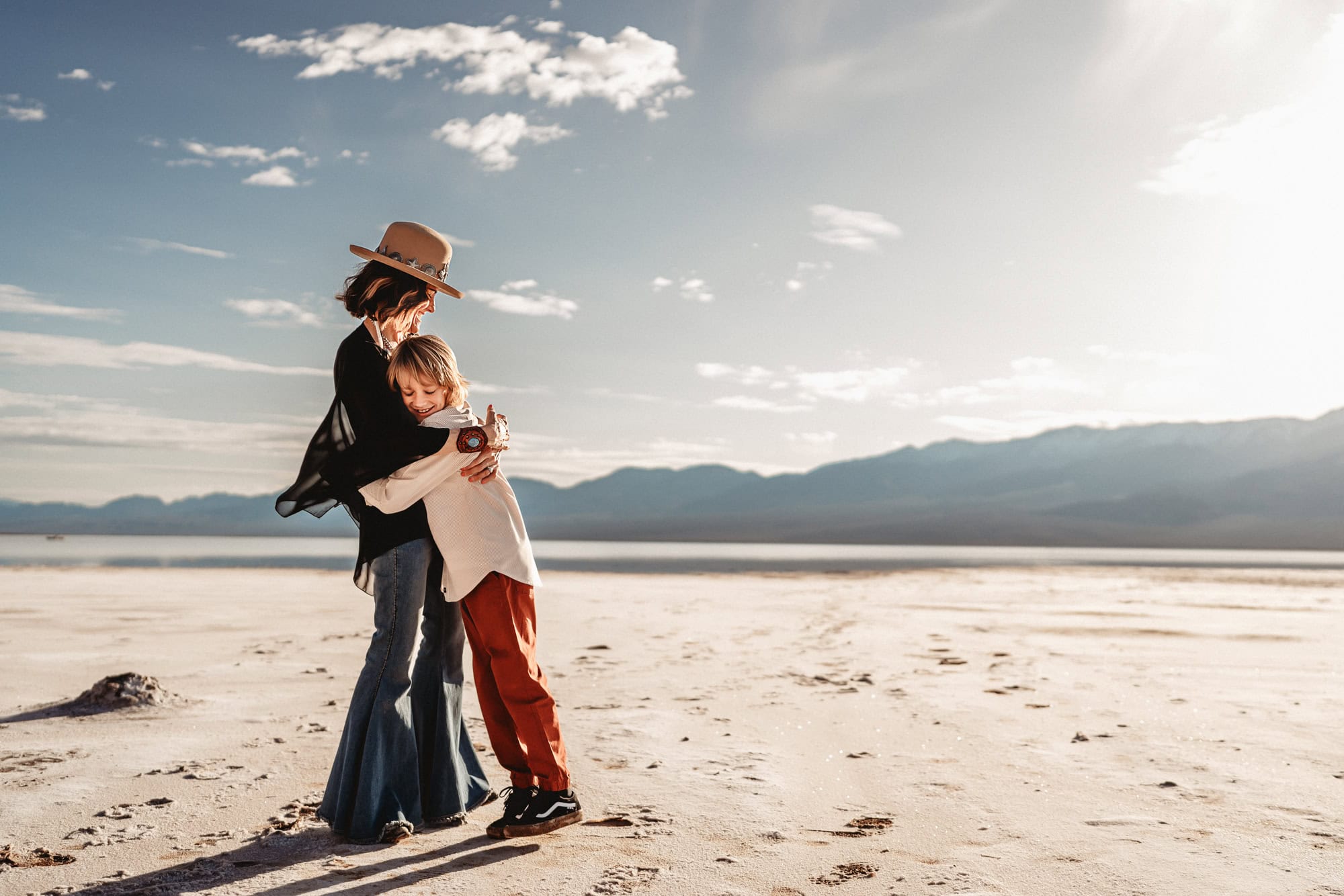 A woman wearing a hat and jeans hugs her ten year old sun in Death Valley's Badwater Basin.