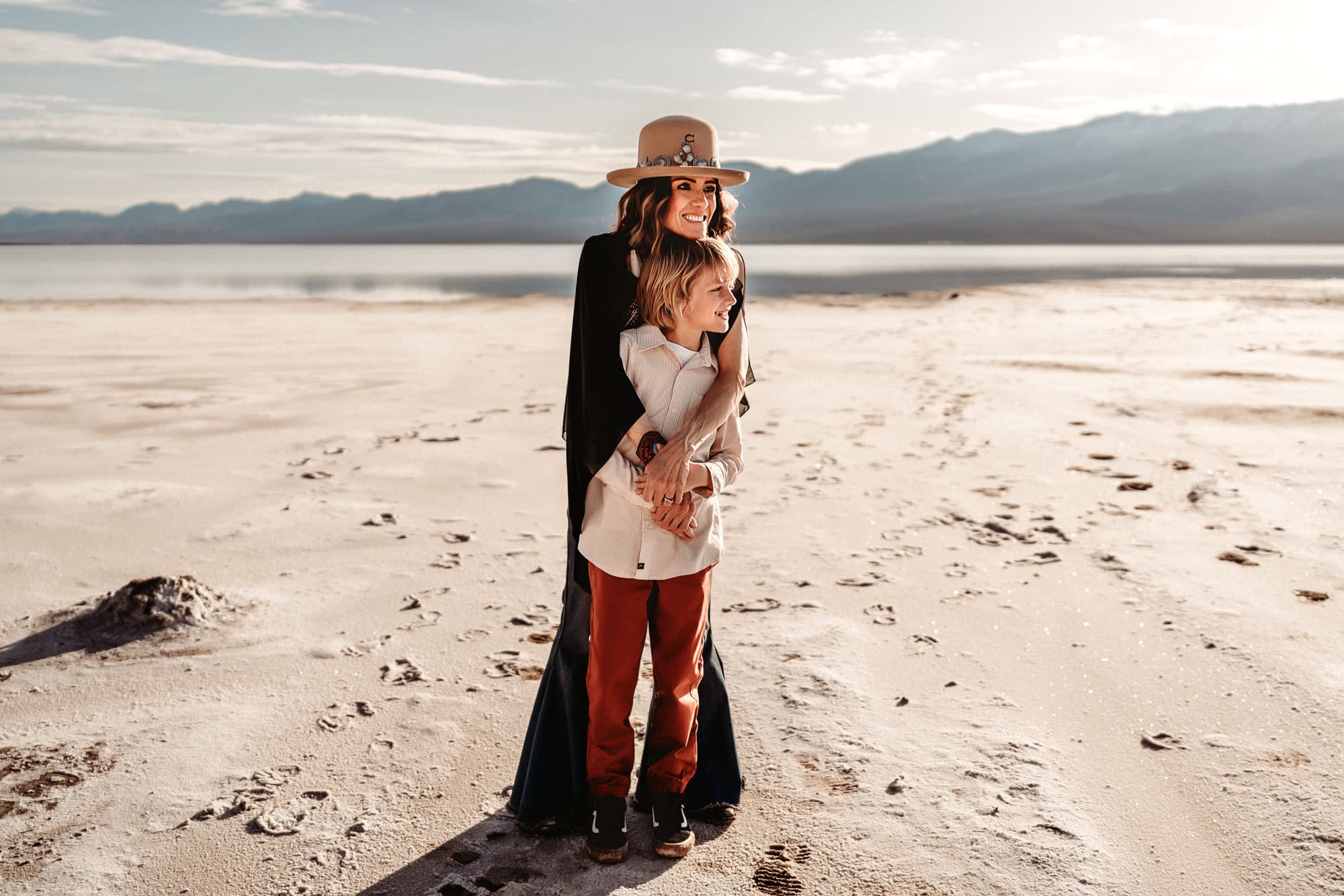 A mom and her ten year old son stand in Death Valley's Badwater Basin, hugging and looking off in to the distance together. This is during a family photo session by San Diego's Love Michelle Photography.