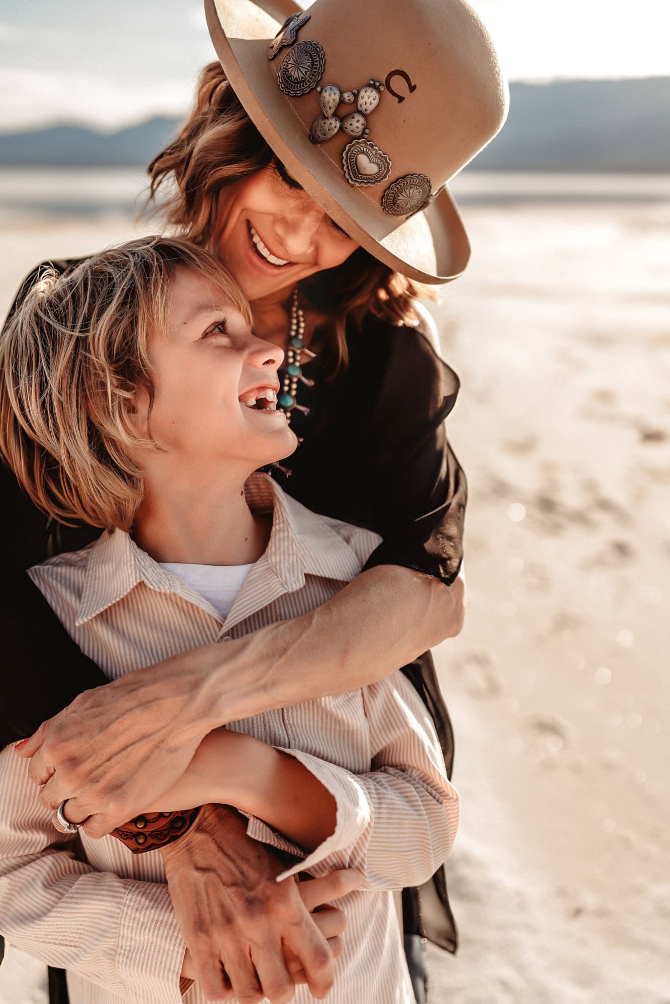 A mom and her 10 year old son embrace and smile at each other  during  a family photo session in Death Valley's Badwater Basin. 