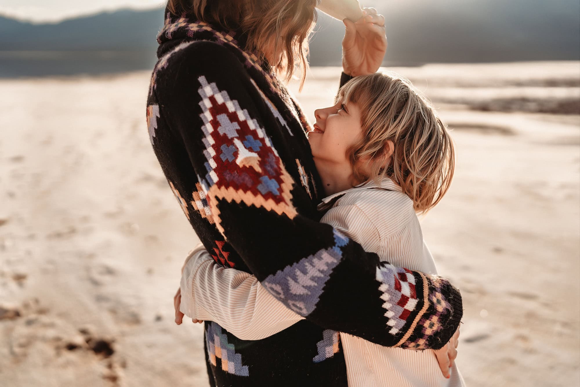 A close up of a woman wearing a cowboy hat, hugging her ten year old son as he looks up at her and smilies, during a family photo shoot in Death Valley National Park.