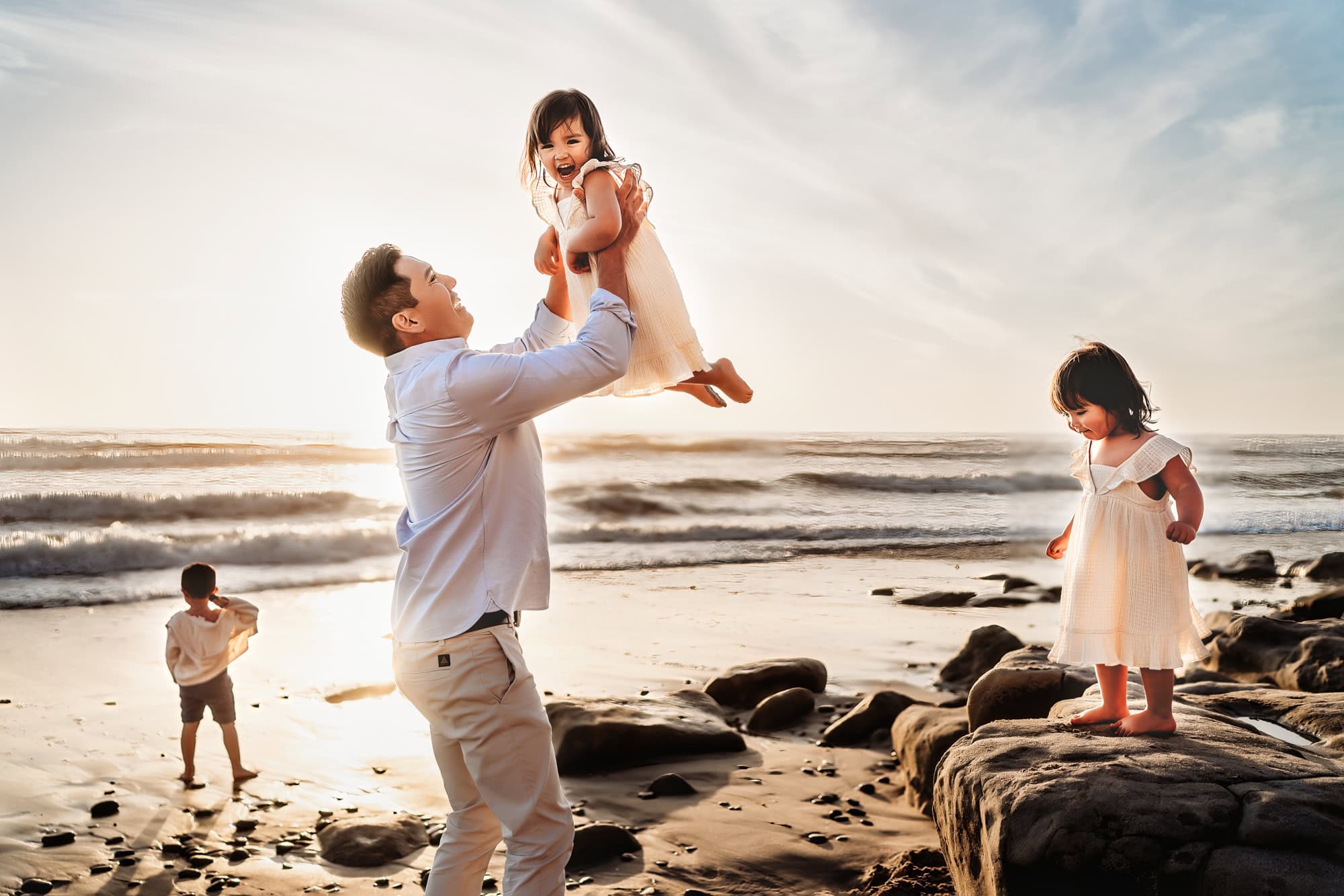 A dad stands on the beach in Del Mar and tosses his little girl in the air while she laughs. 