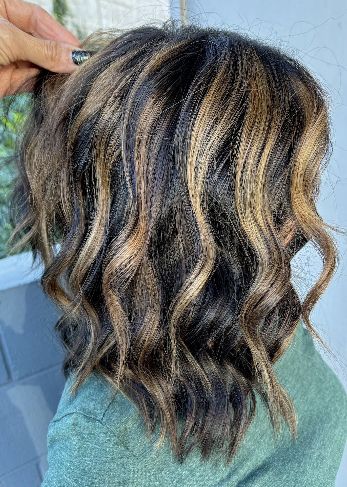 The side of a brunette woman's head is visible, showing the balayage hair coloring method, in an article about a San Diego hairstylist. 