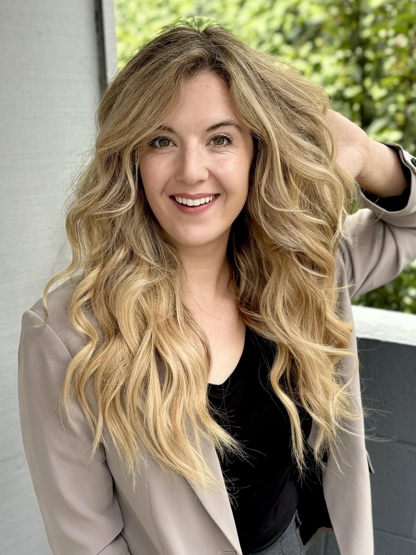 A smiling blonde woman shows her hand tied extensions in an article about San Diego hairstylist Mishawna Romero Hair.