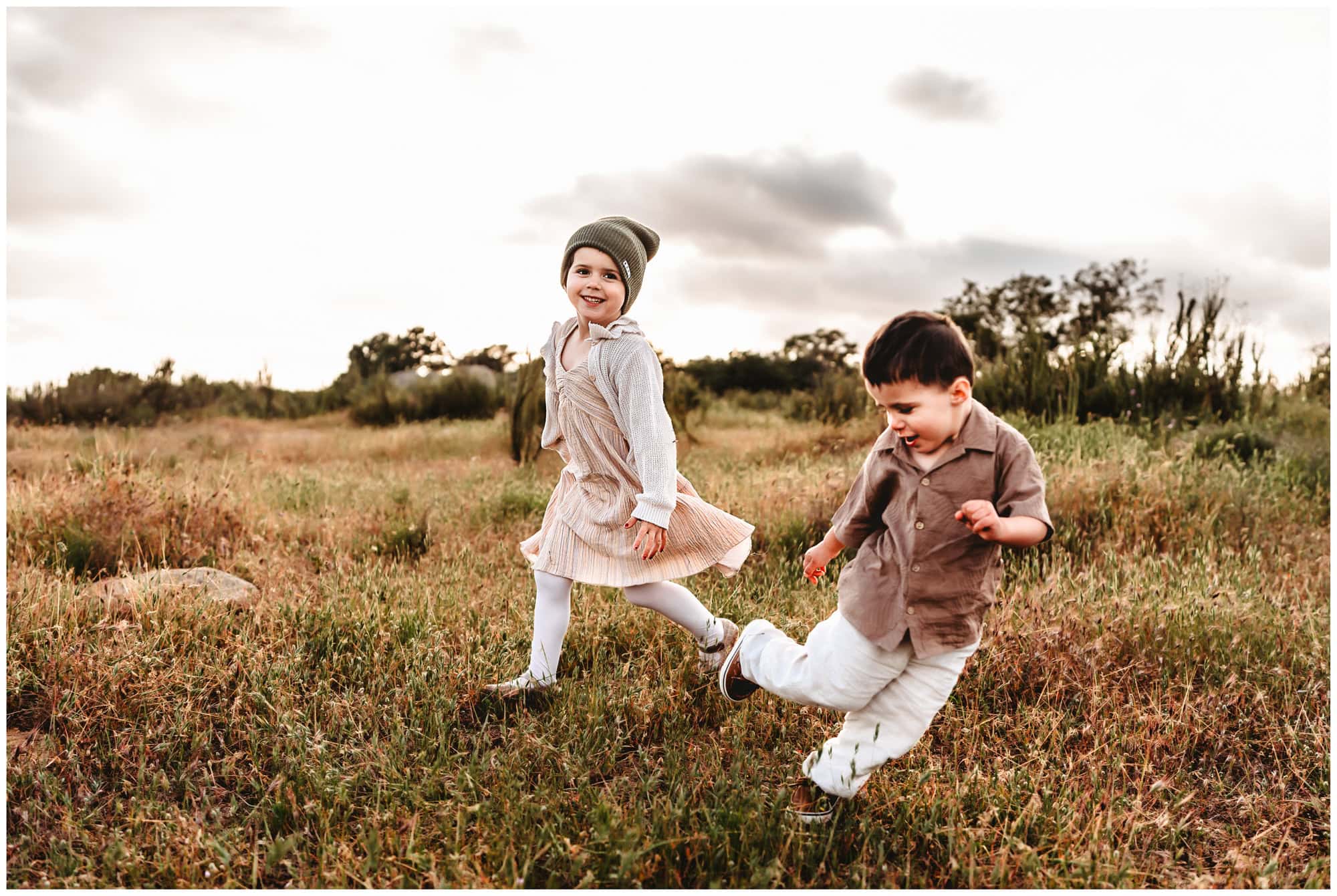 A little girl and her toddler brother run around with big smiles on their faces, in a San Diego field during a family photoshoot. 