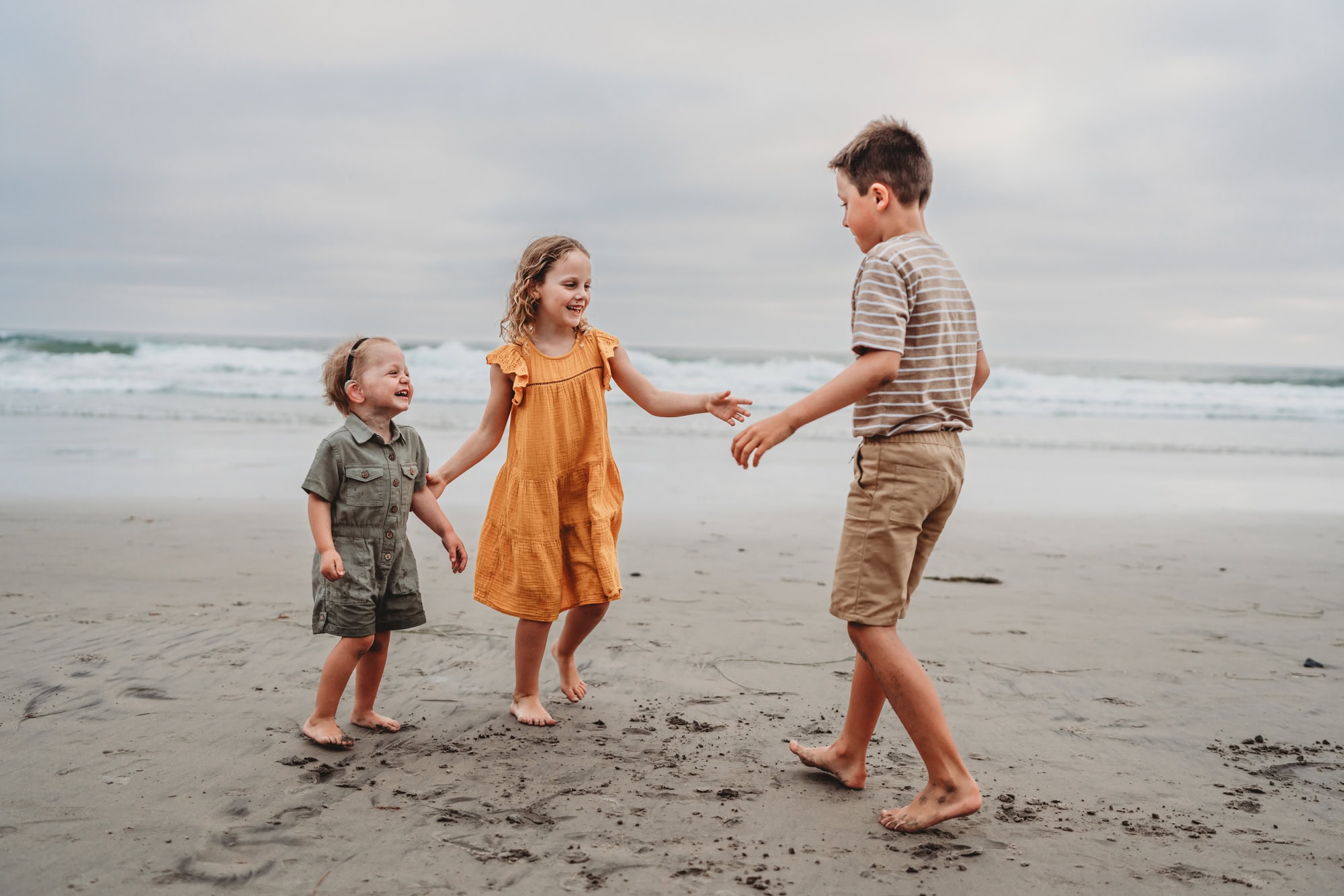 Three siblings play in the sand on a beach in Del Mar, California