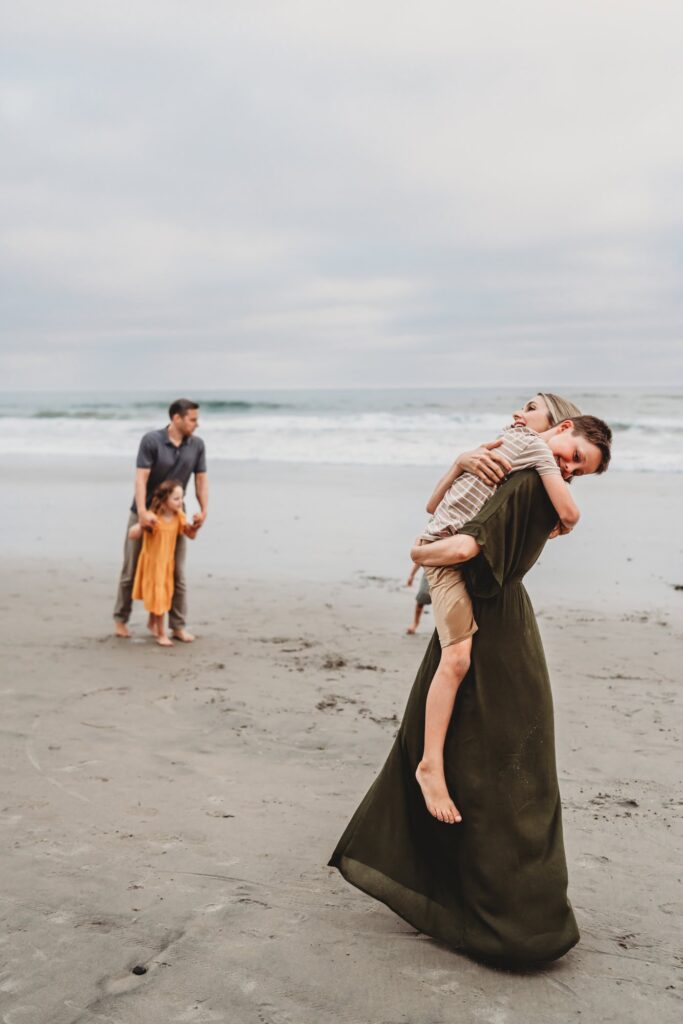 San Diego Family Photographer captures mother hugging child while father plays with other children in ocean