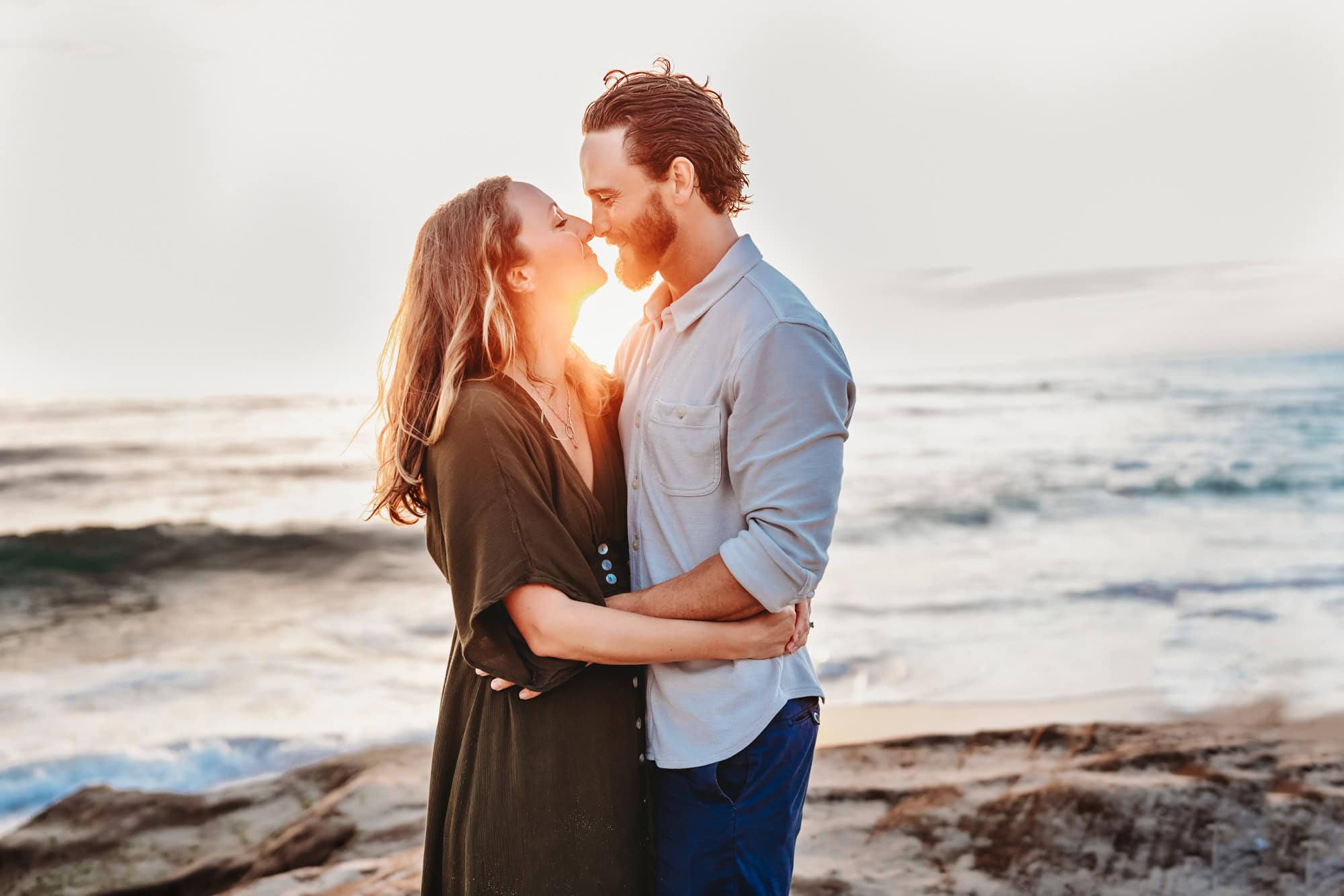 A man and woman smile and touch noses during a family photoshoot on La Jolla's Windansea Beach.