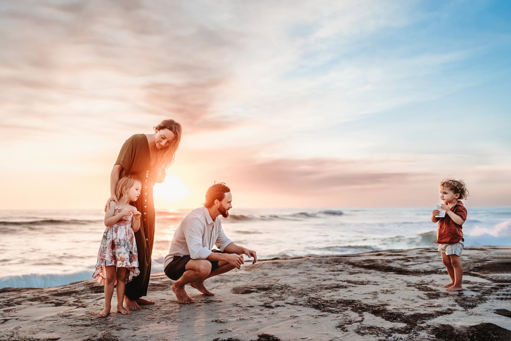 A family stands on a rock on Windansea Beach during a family photoshoot.