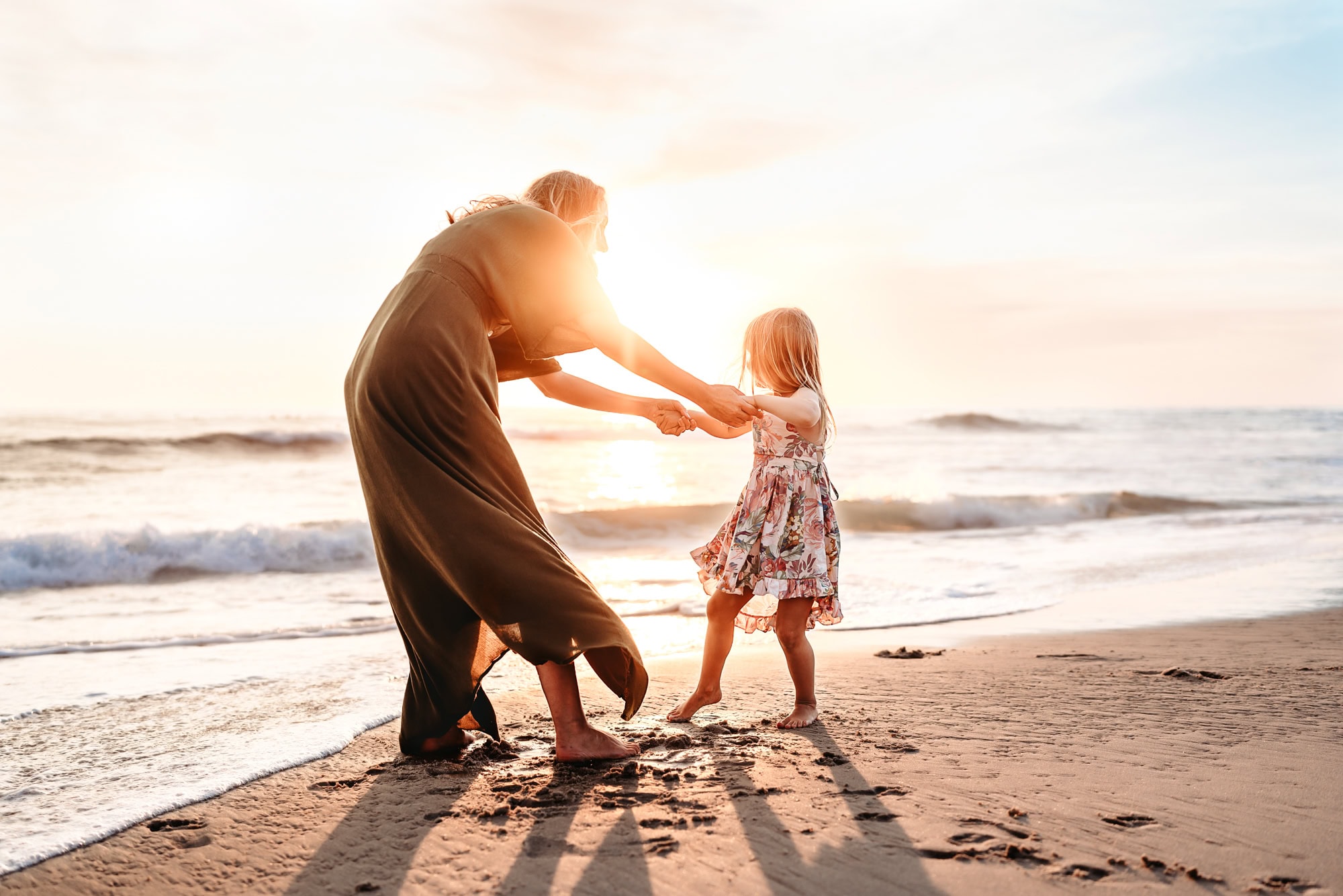 A woman holds her little girl's hands, playing "ring around the Rosie," during a family photo session on Windansea Beach.