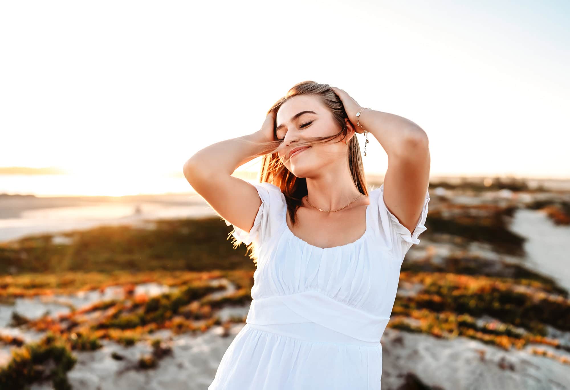 A young woman hold her hair back and smiles during a senior photoshoot in San Diego.